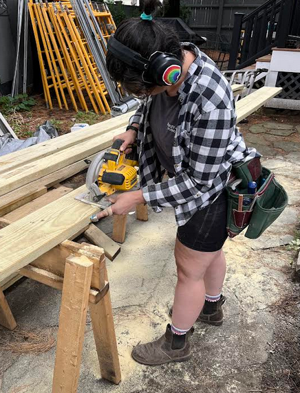 A person cutting a piece of wood with a circular saw in a backyard workshop.
