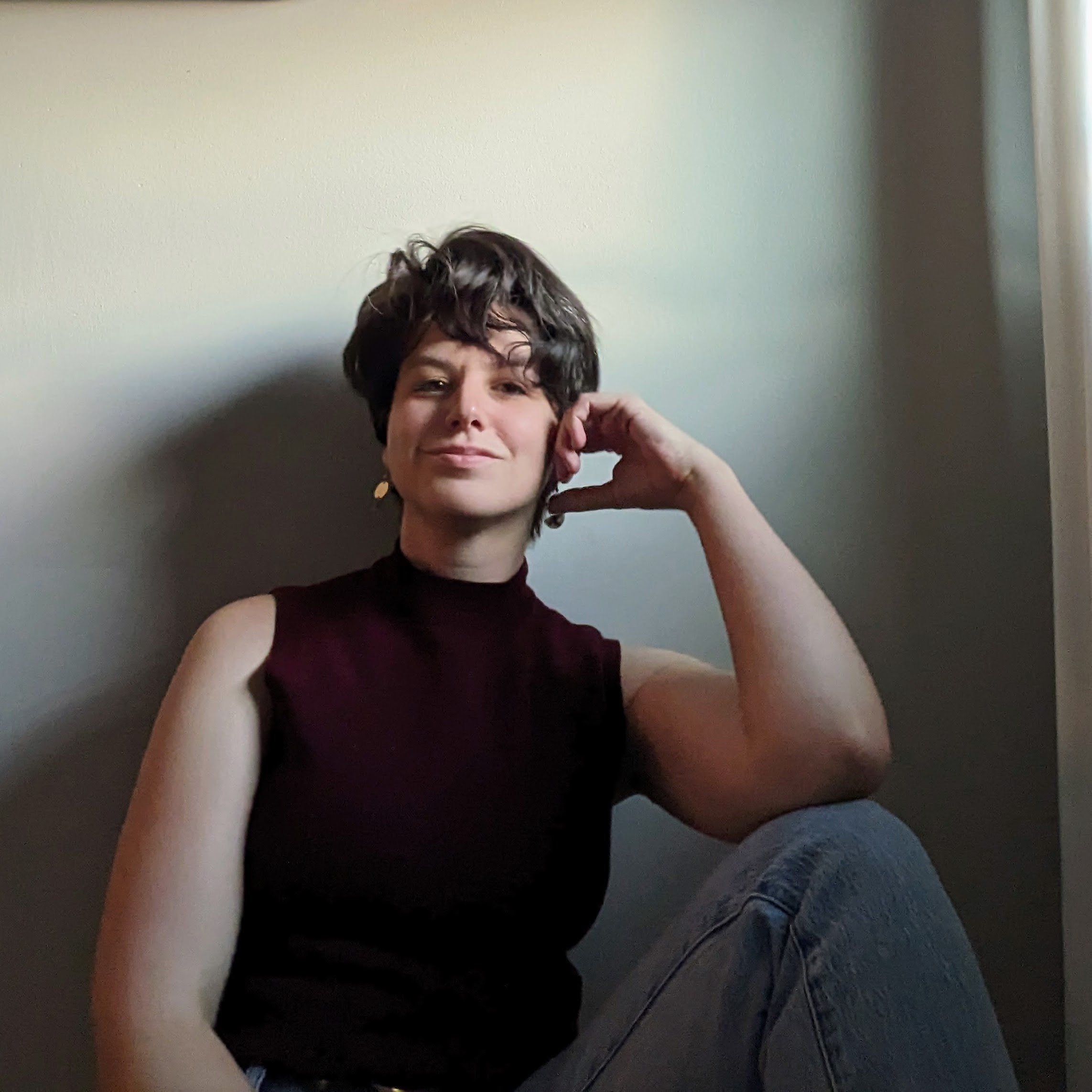 Ginny in a red tank top sitting on the ground with her elbow resting on her knee