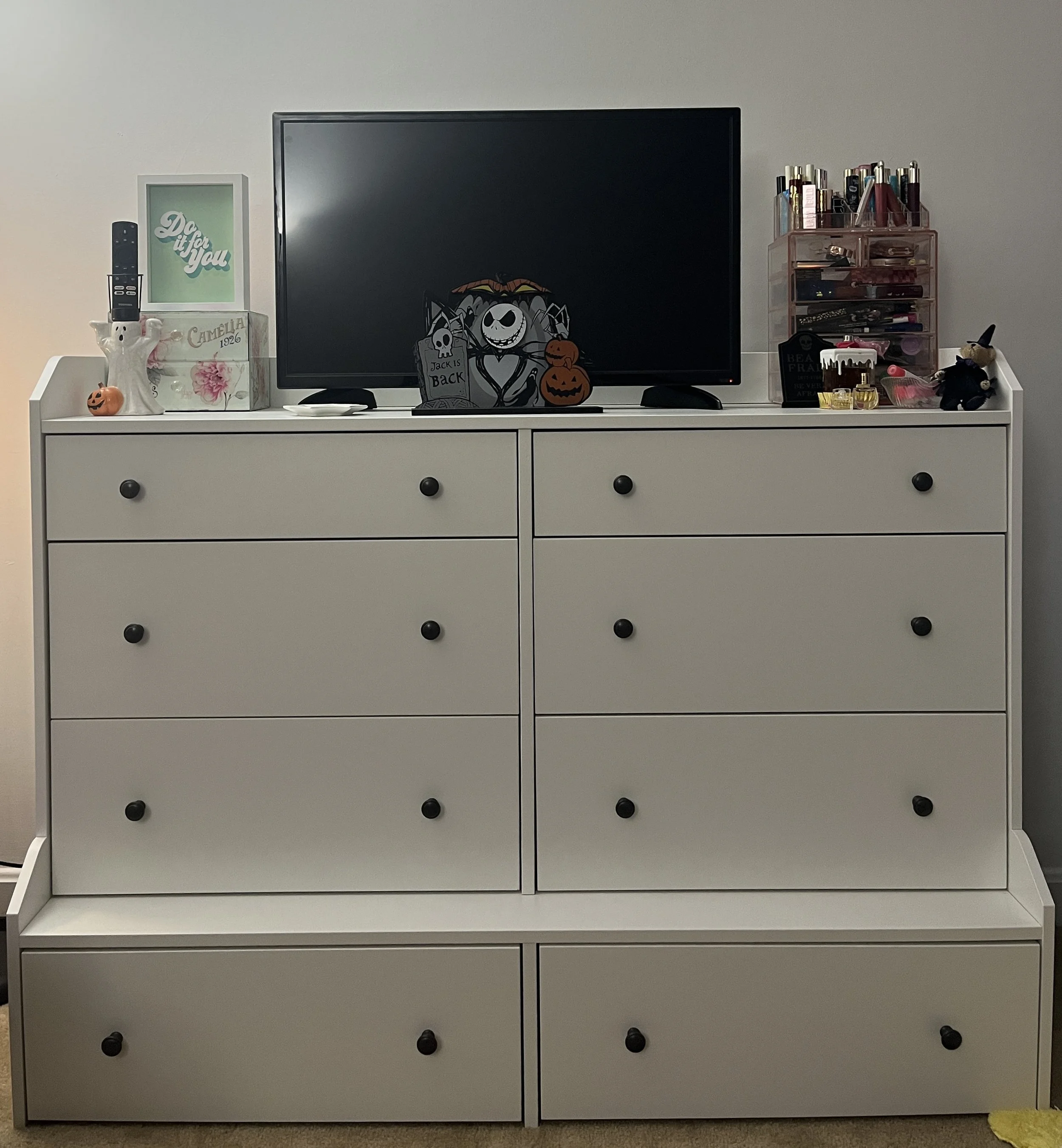 White dresser topped with a TV, Halloween decorations, a small makeup organizer, and miscellaneous items.