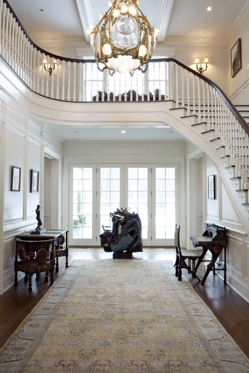 Interior view of a bright, elegant entryway with a staircase, chandelier, and French doors.