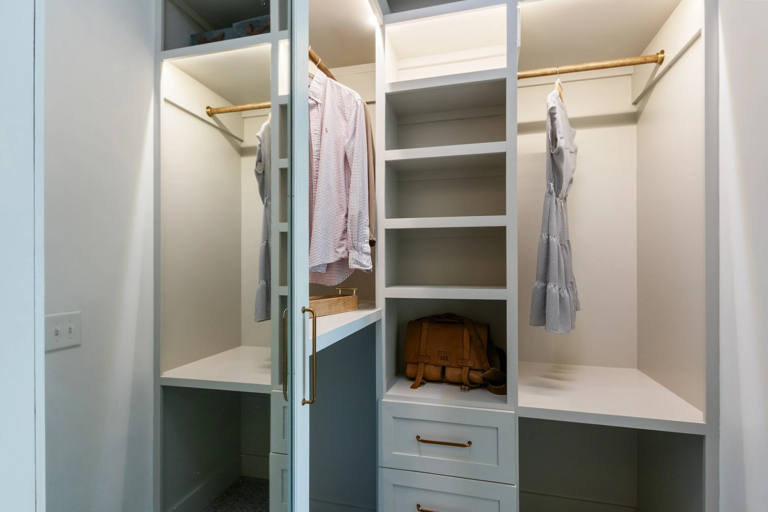 Empty white closet with hanging rods, shelves, and drawers, containing a brown briefcase and a few clothing items.