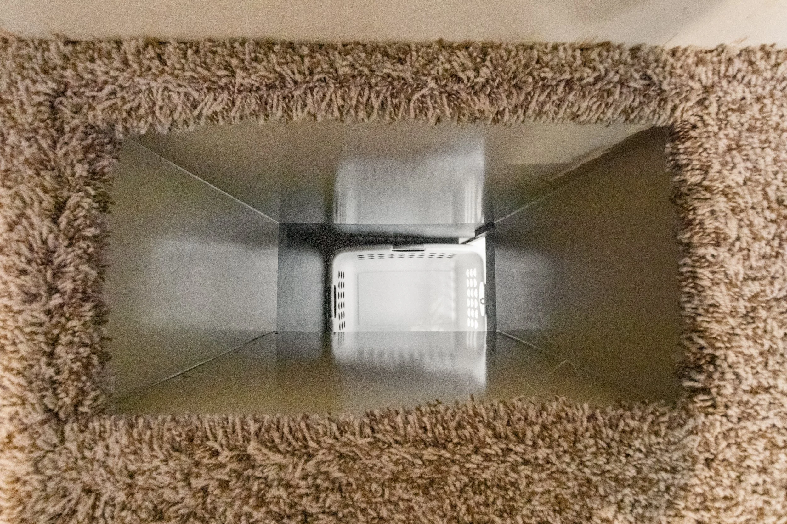 Empty metal tissue box holder with a rectangular opening, viewed from above with a beige carpet surrounding it.