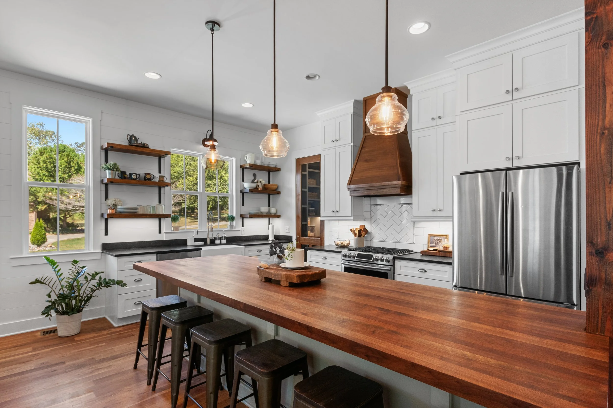 Modern kitchen with white cabinets, black countertops, stainless steel refrigerator, wooden island with stools, open shelves, and pendant lights.