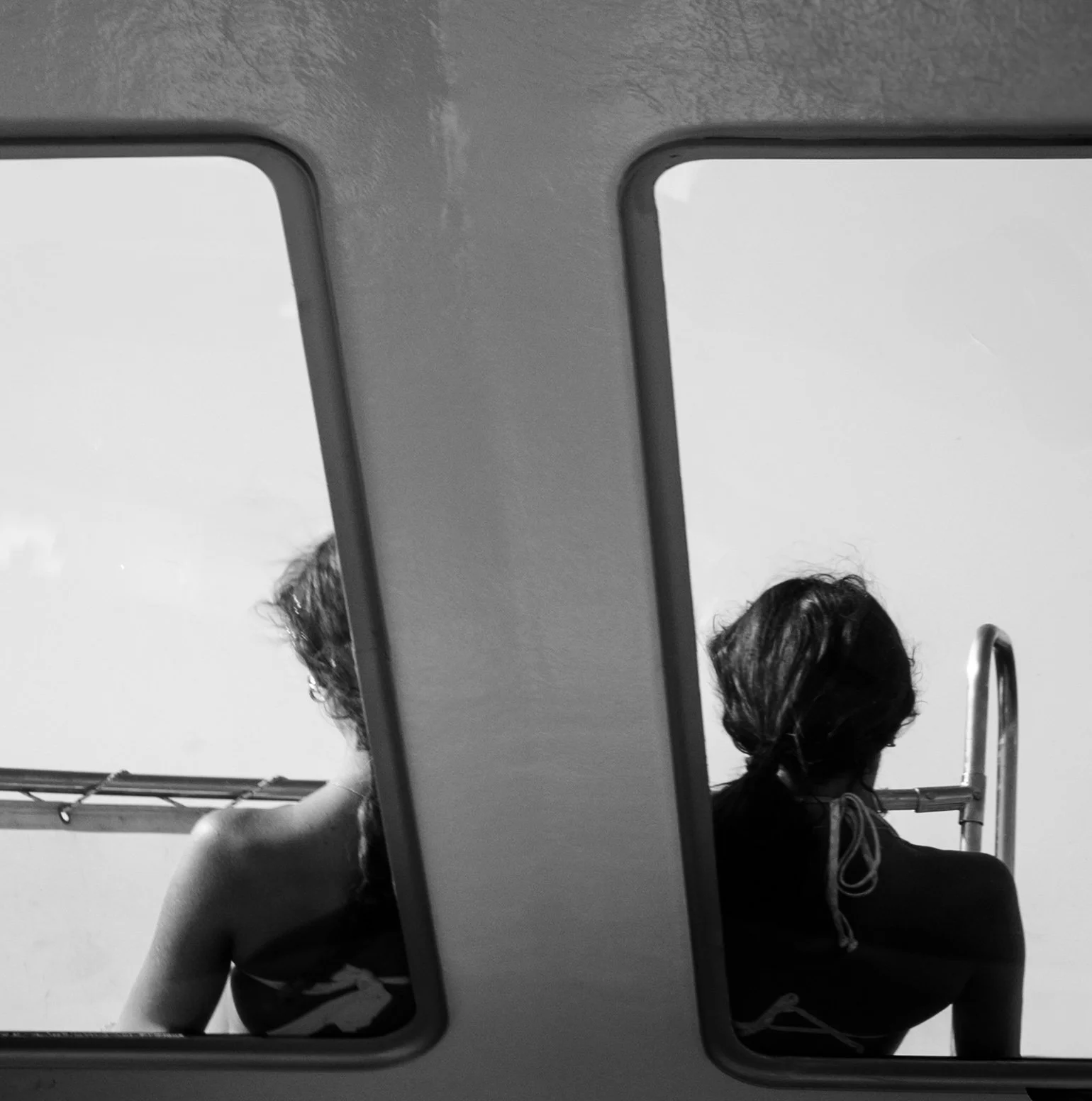 A woman with wavy hair sitting near a railing, reflected in two adjacent bus windows.