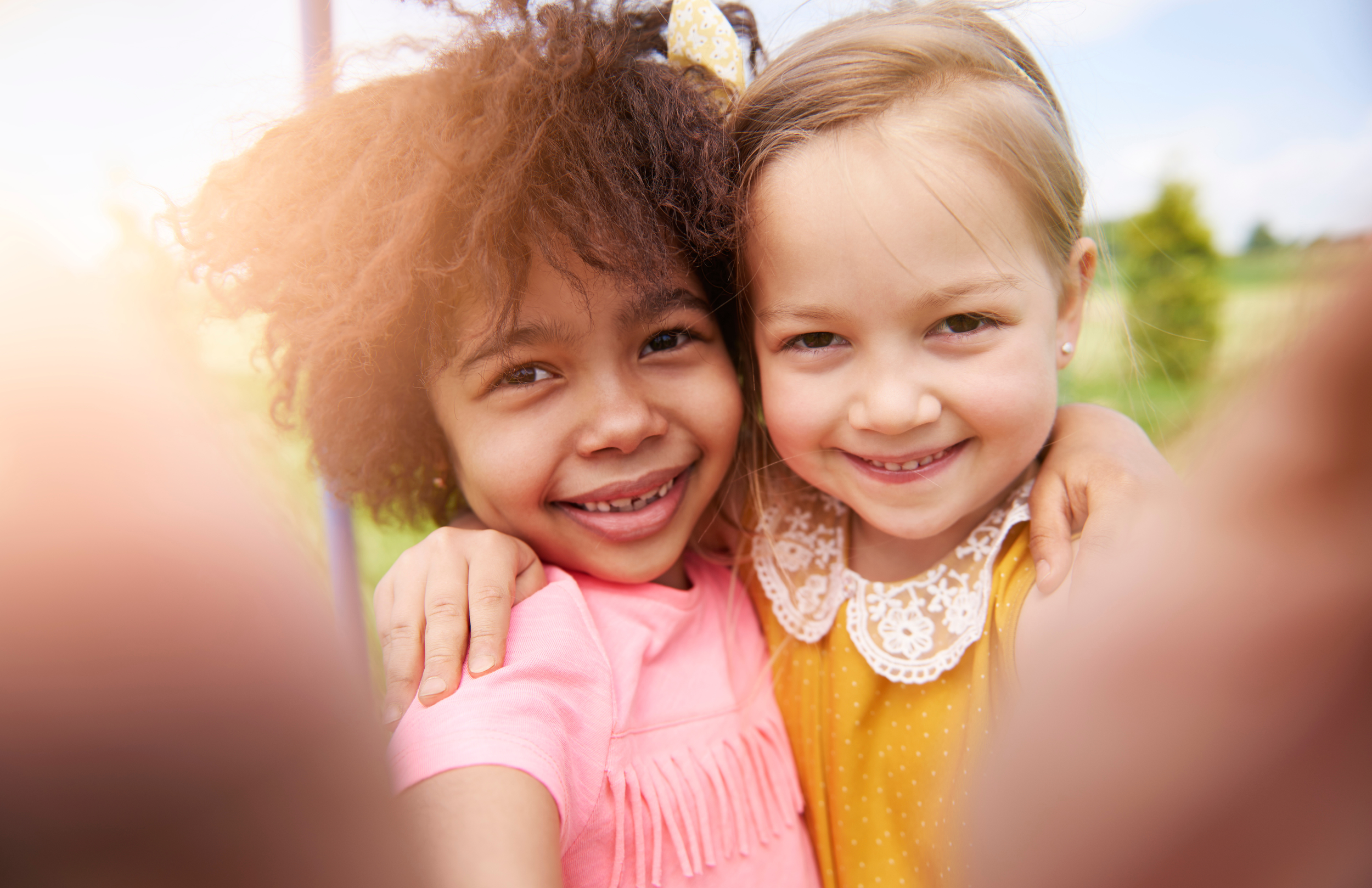 Two young girls smiling and hugging each other outside, taking a close-up selfie. Safe and clean indoor play center for families in Howell MI.