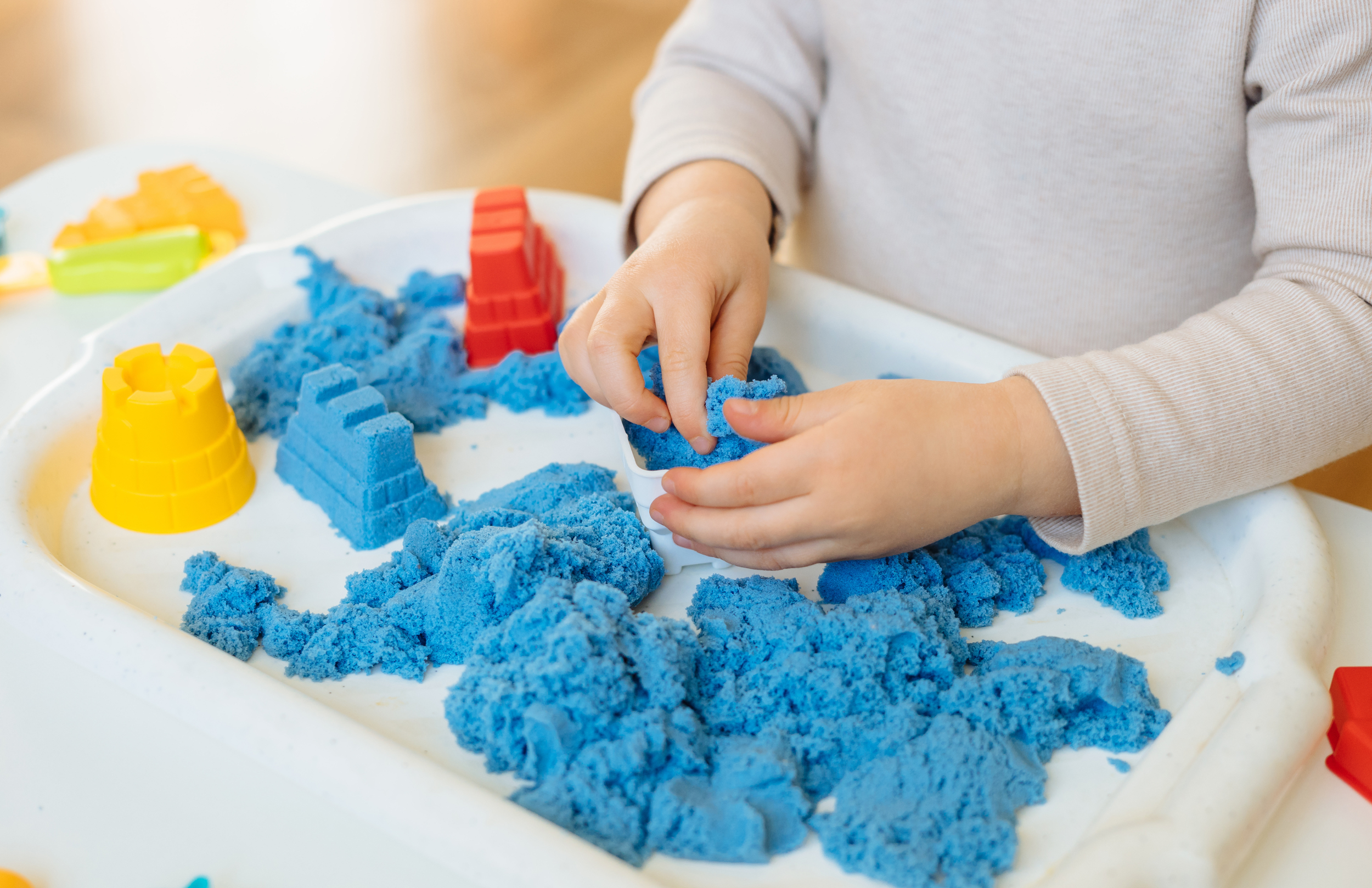 Child playing with kinetic sand in a tray, using colorful molds and tools. Sensory play equipment for children in Livingston County, Michigan.