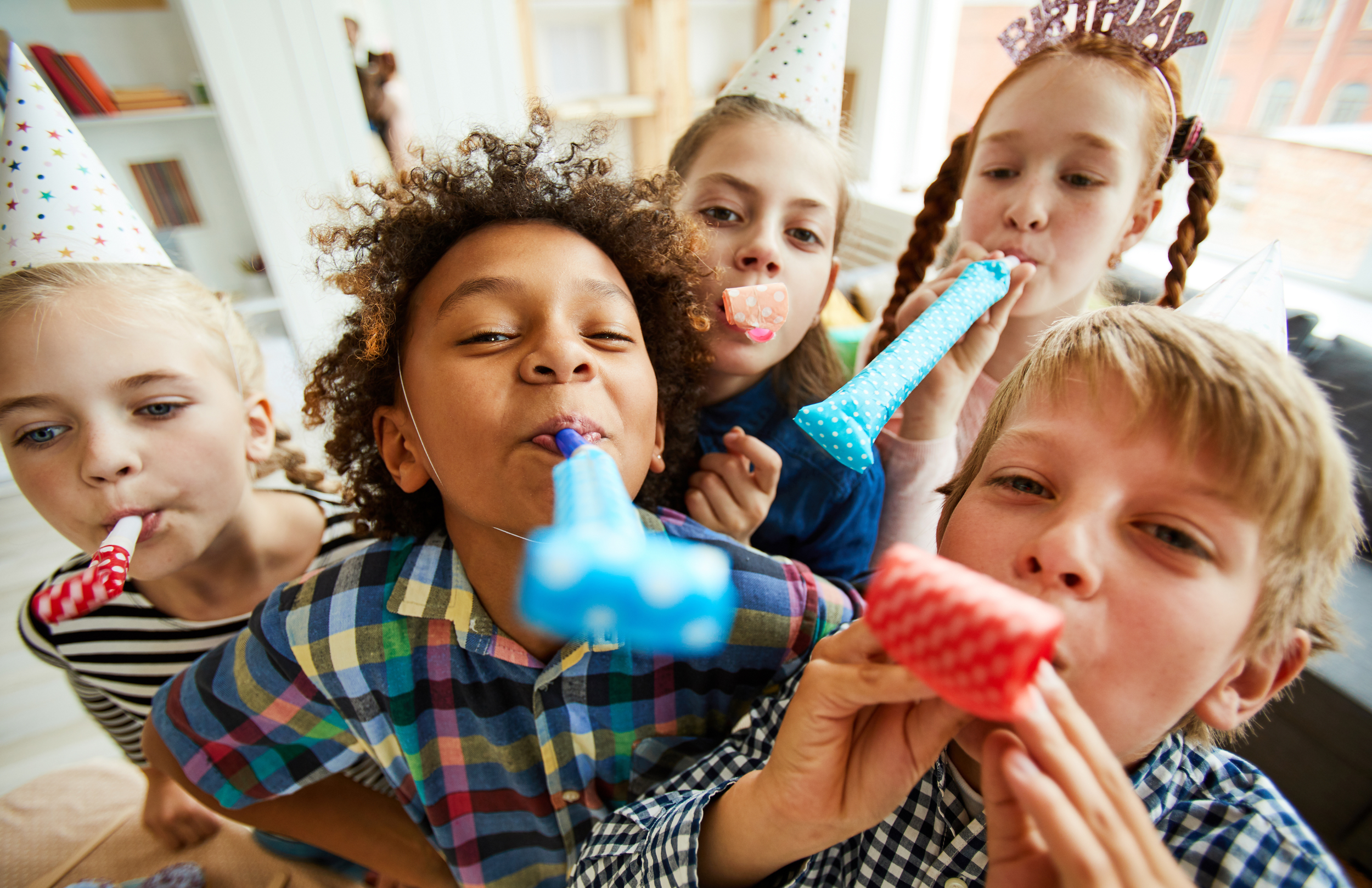 Children celebrating birthday wearing party hats and blowing party blowers at a party. Kids birthday party setup at indoor play place in Howell MI.