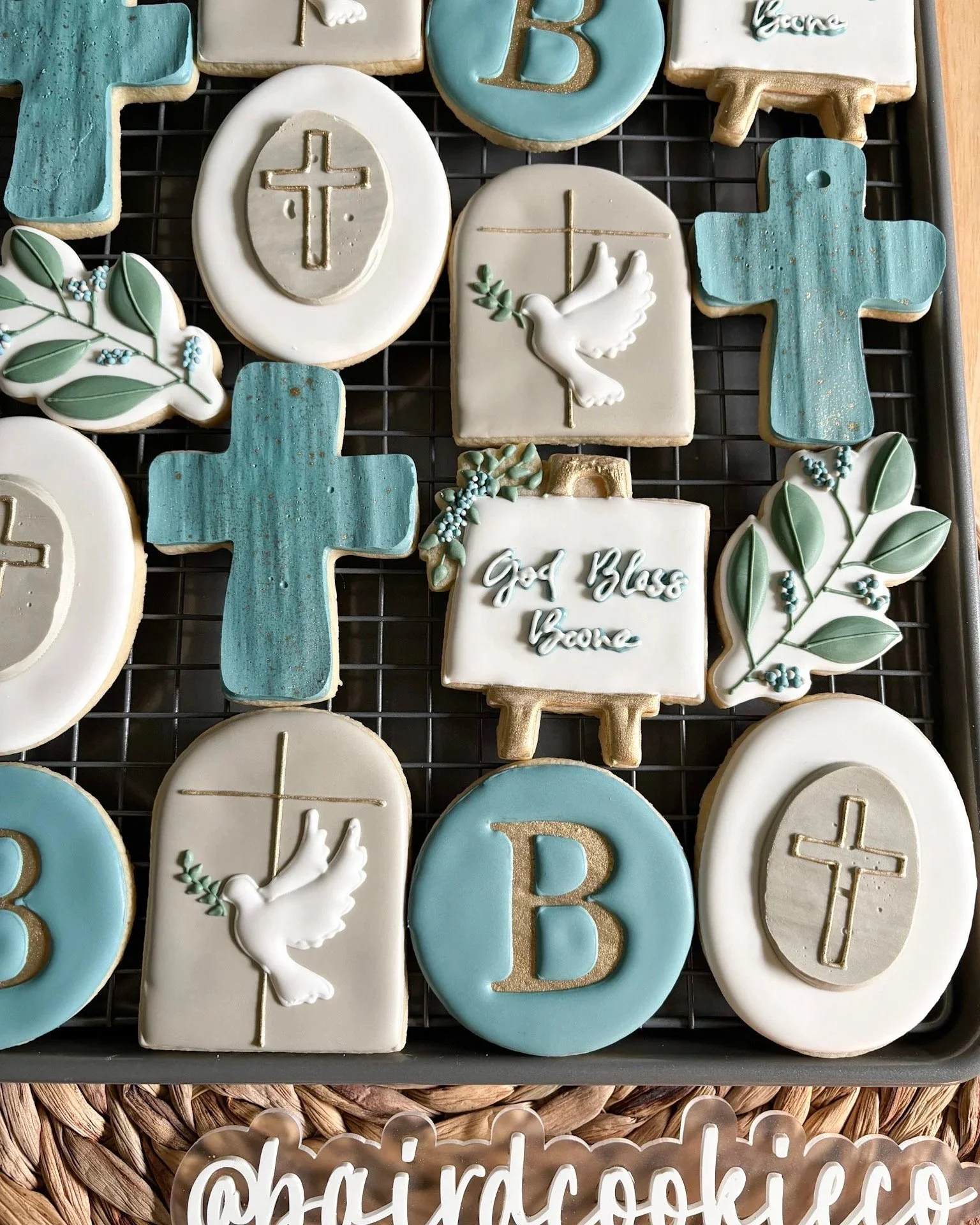 Collection of religious-themed cookies decorated with crosses, doves, the words 'God Bless' and leafy accents, in blue, white, and gold colors.