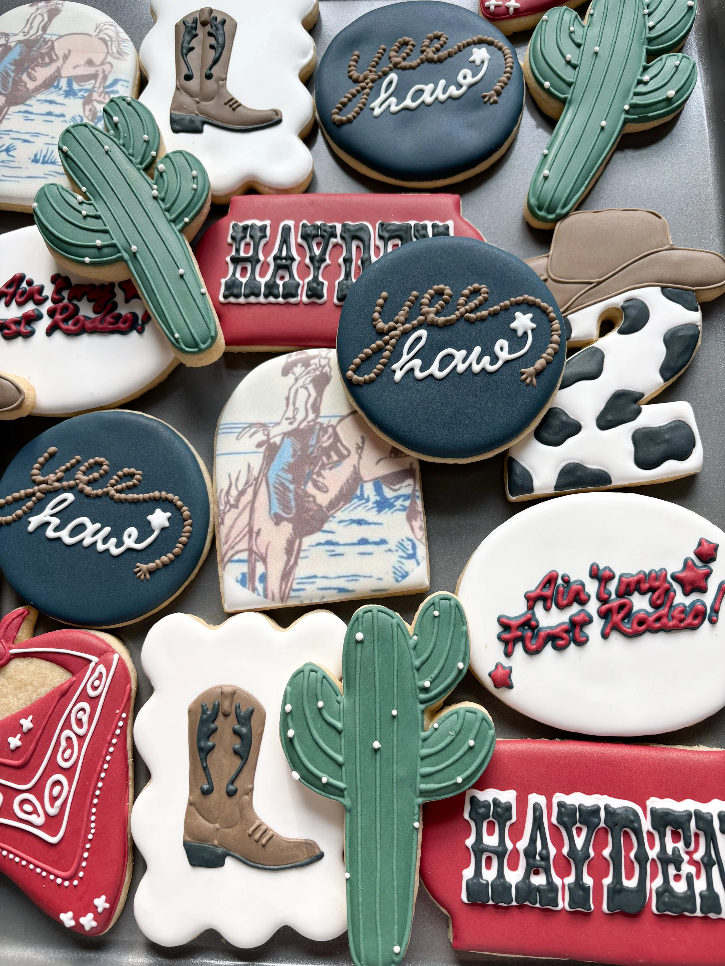 Assorted rodeo-themed cookies, including cacti, cowboy boots, cowboy hats, horses, and text reading "Yee Haw" and "Hayden."