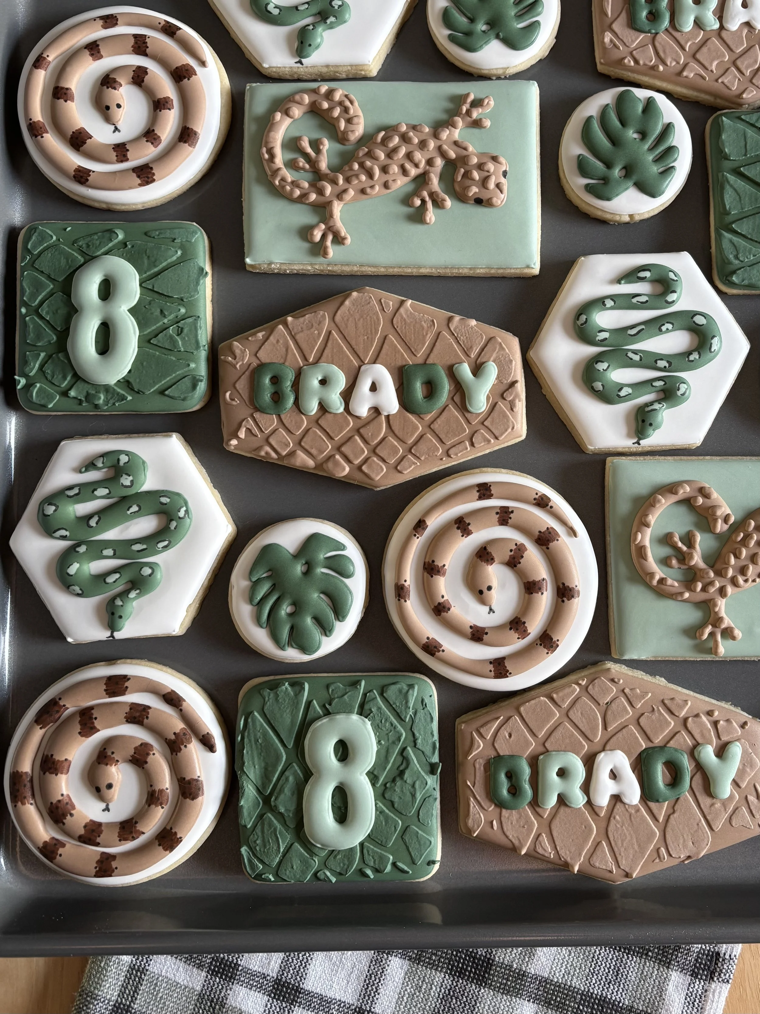 Decorated cookies with animal themes, numbers, and the name 'Brady' in various shapes and colors.