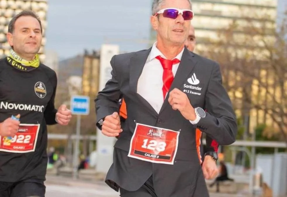 Hombres corriendo en una competencia con números en sus camisetas, uno con traje y corbata y el otro con ropa deportiva.