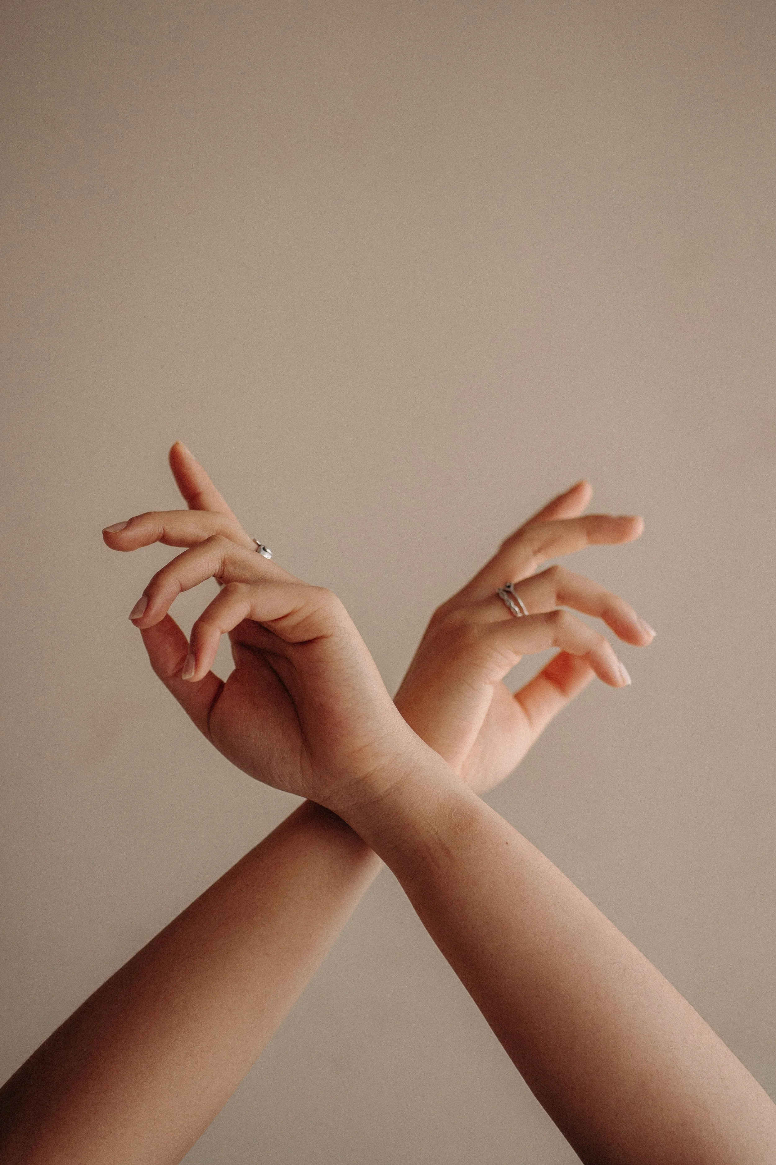 Two hands with fingers forming delicate gestures against a plain beige background.