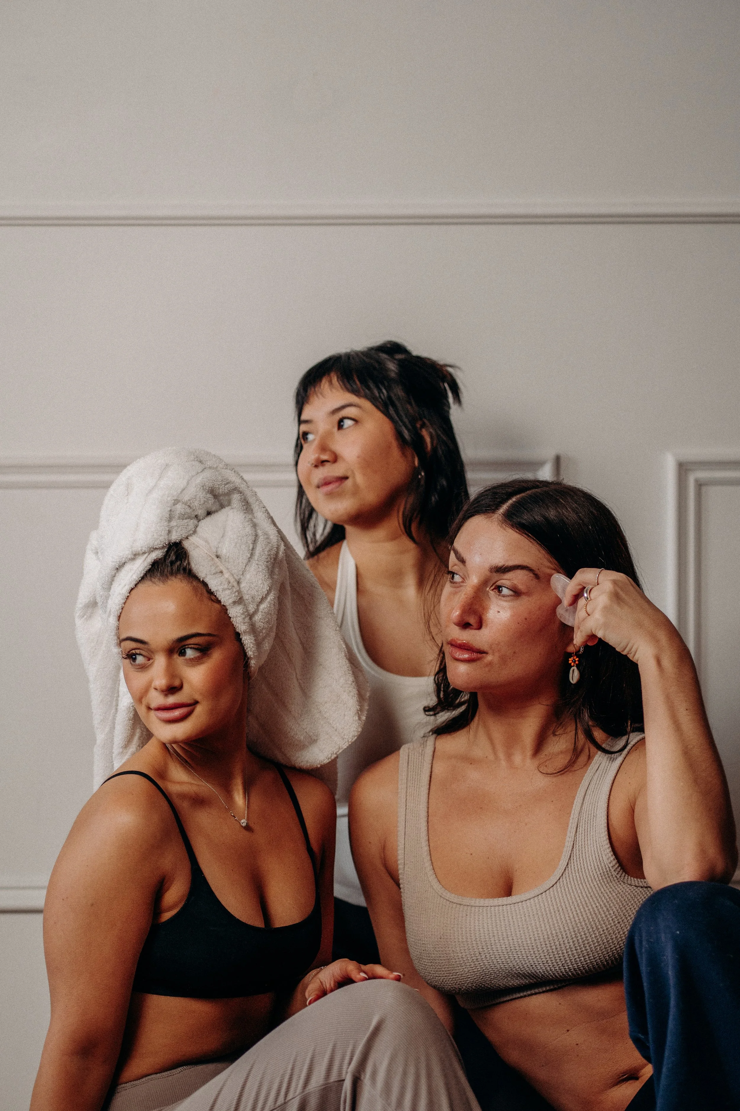 Four women sitting together, one with a towel wrapped around her head, another looking to the side, and two appearing to be chatting, in a casual indoor setting.