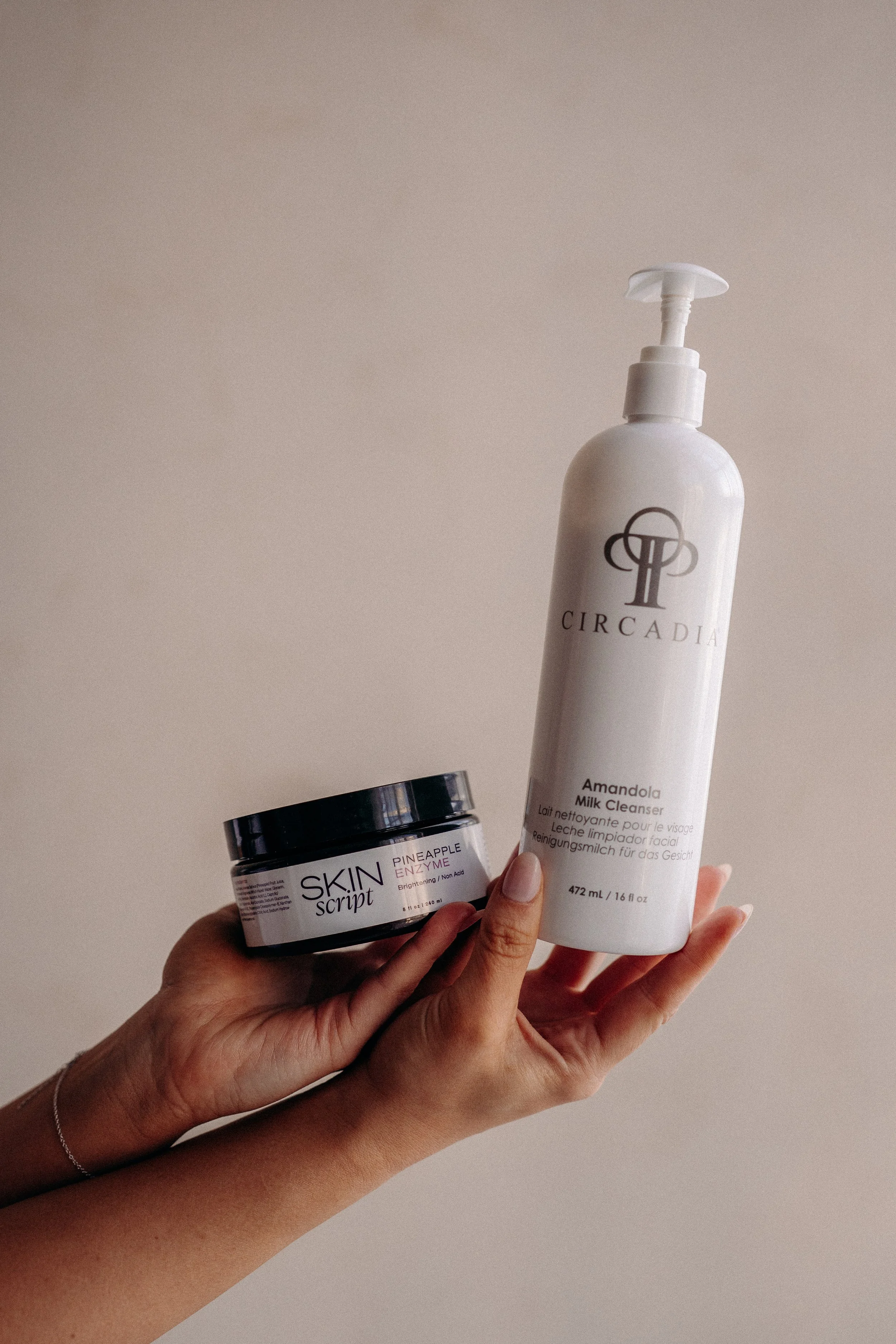 A person holding skincare products, including a white bottle labeled 'CIRCADIA' and a small jar labeled 'SKIN Script' with the text 'Pineapple Enzyme' on it.