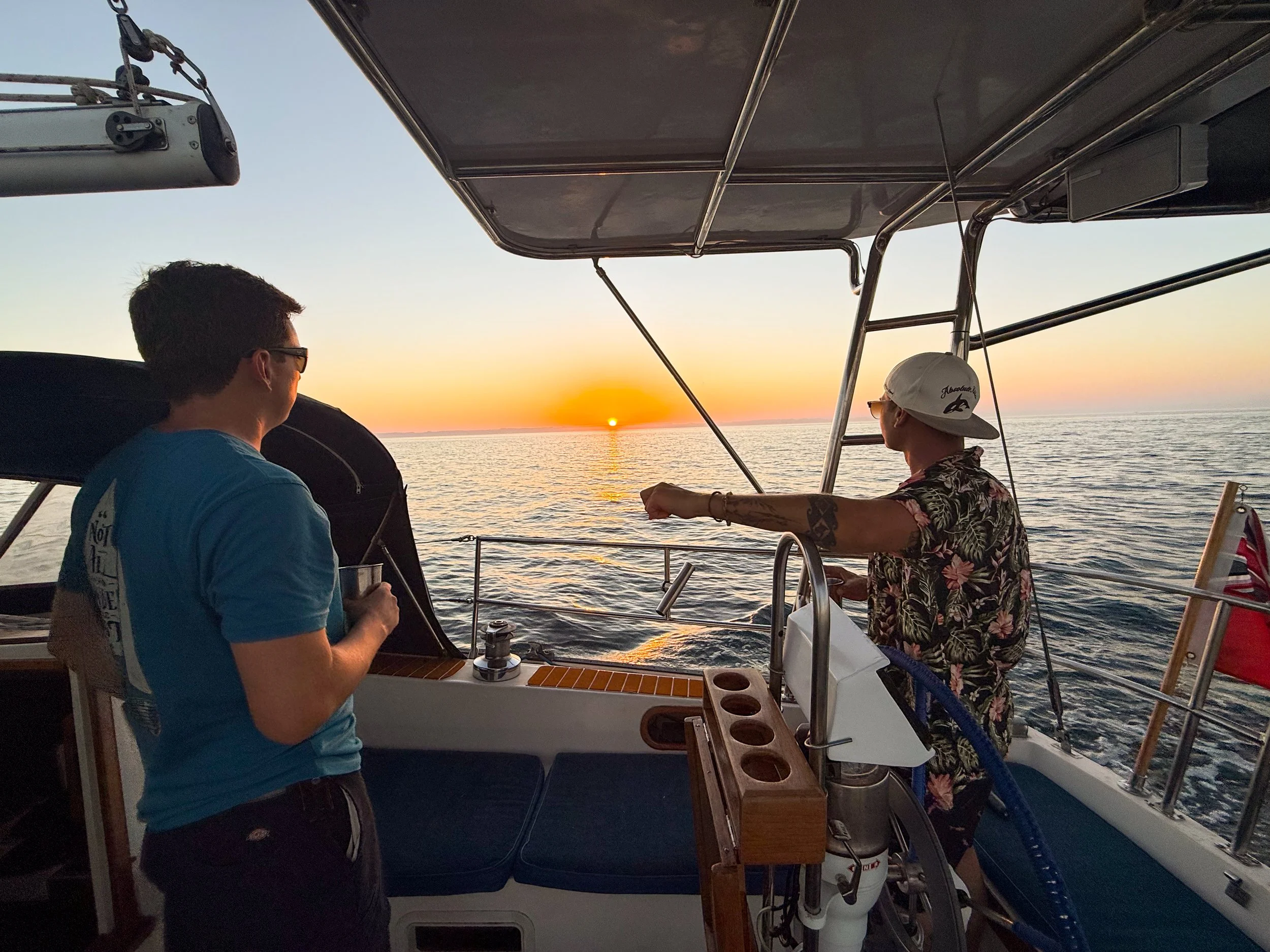 Two men on a boat watching a sunset over the ocean.