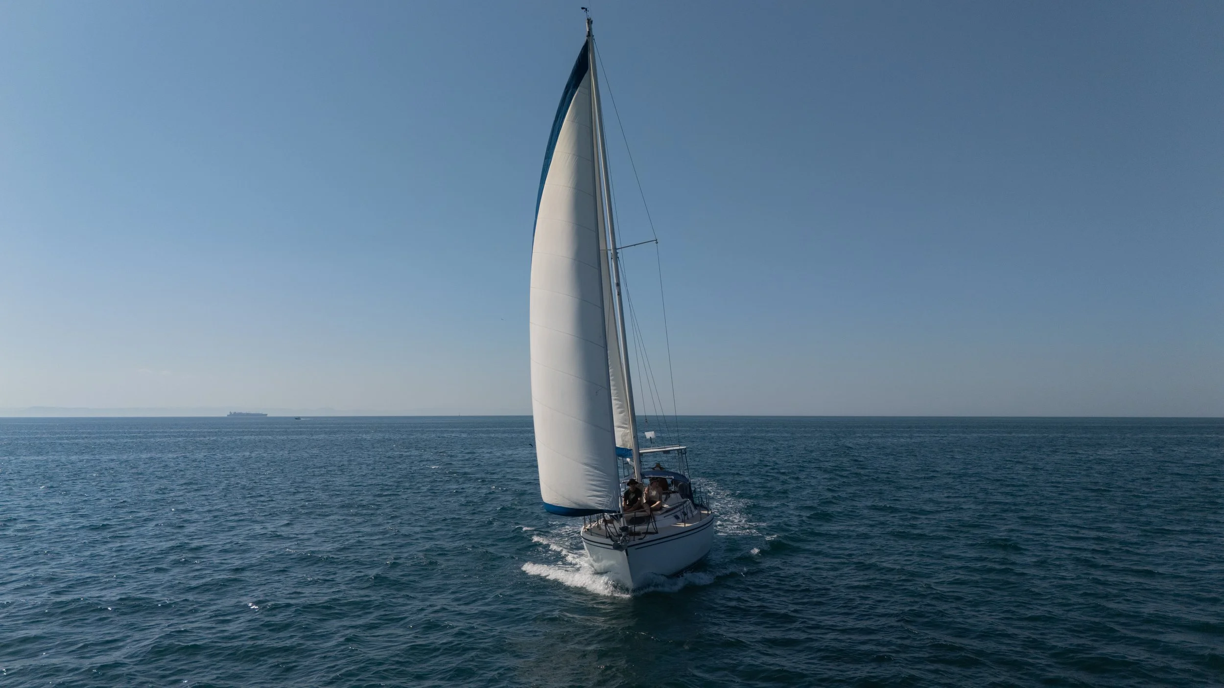 A sailboat with white sails moving across a calm blue ocean under a clear sky.