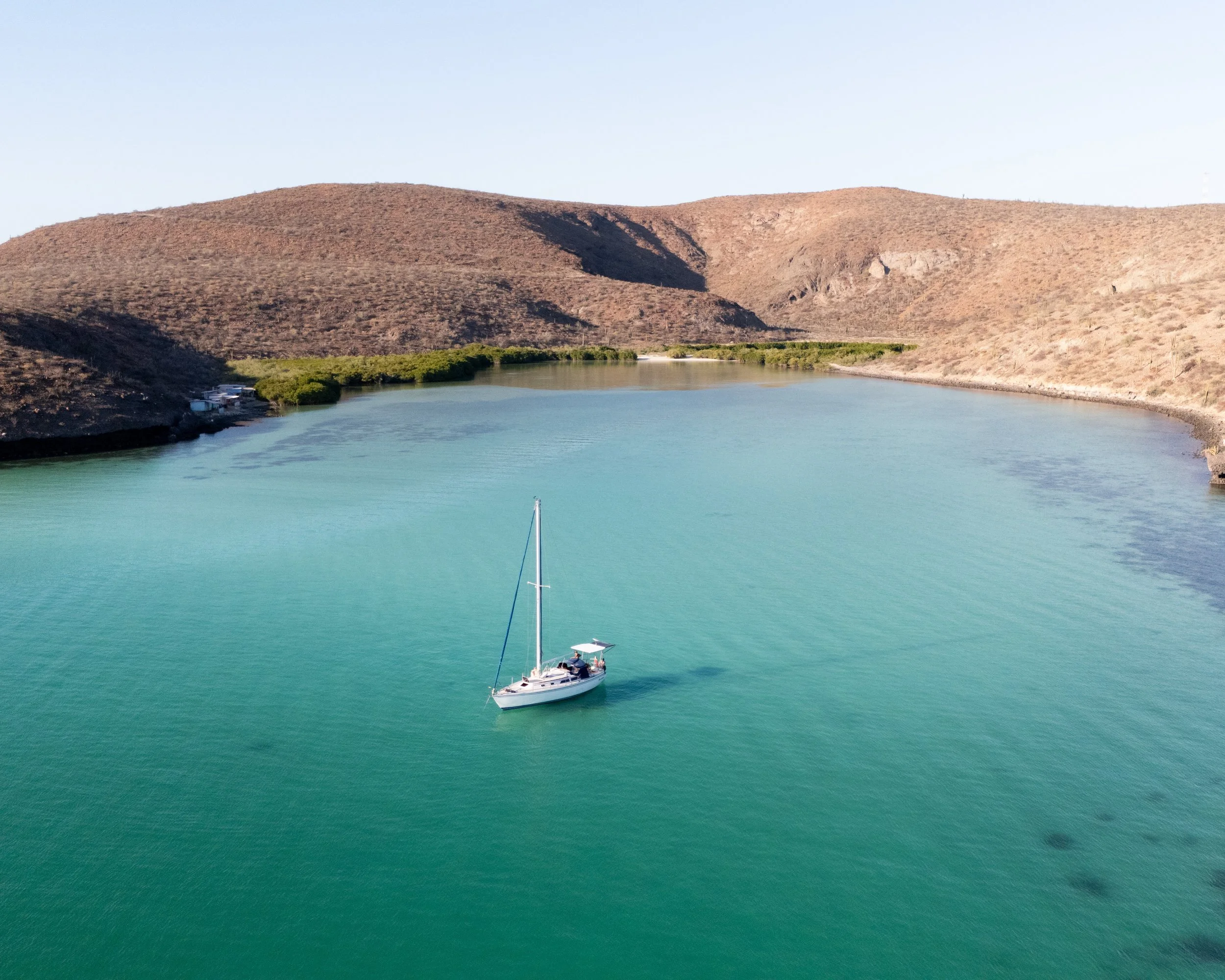 A sailboat on calm turquoise water near arid hills with sparse vegetation.