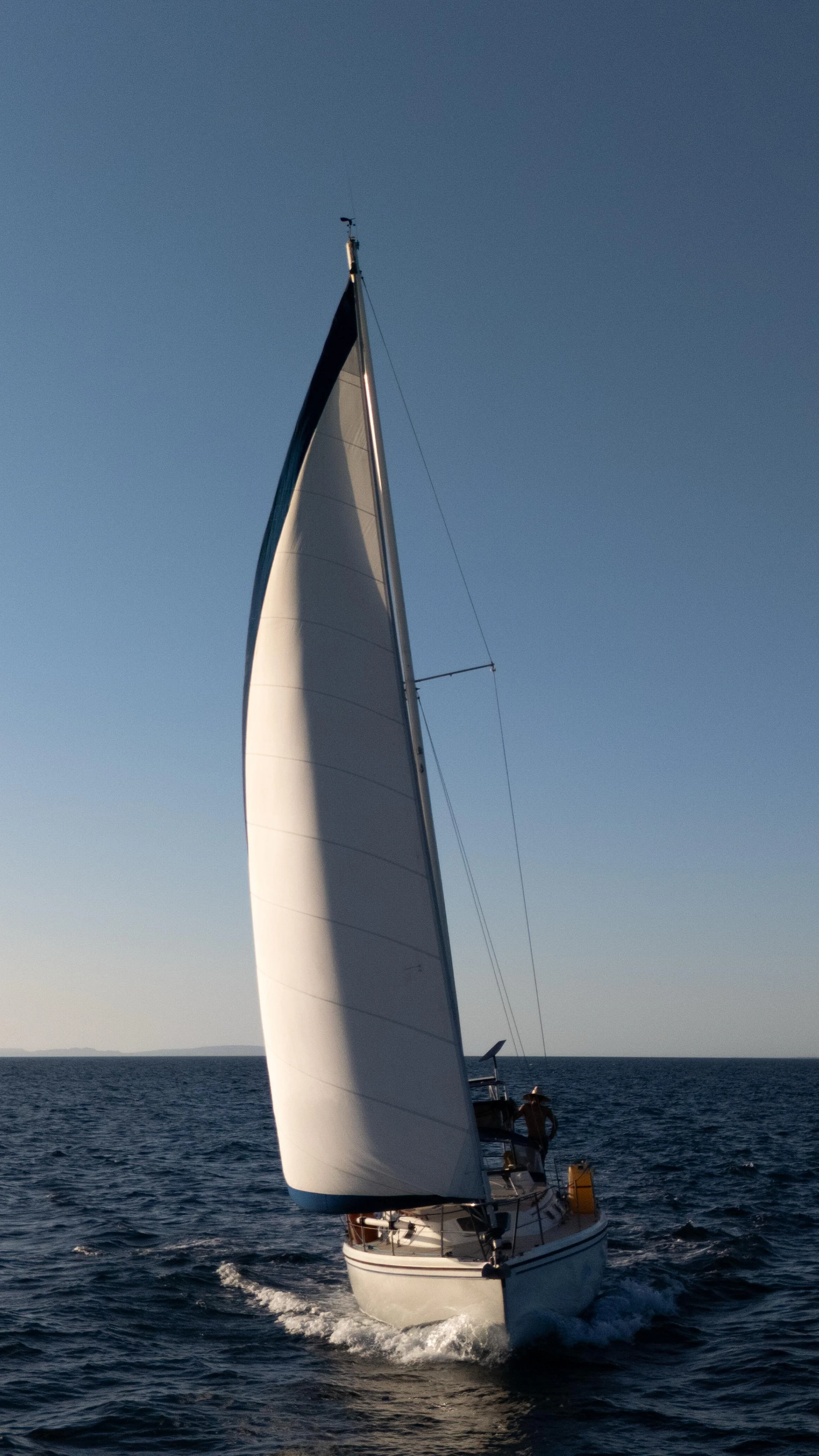 A sailboat with white sails on the ocean during sunset, with a clear blue sky.