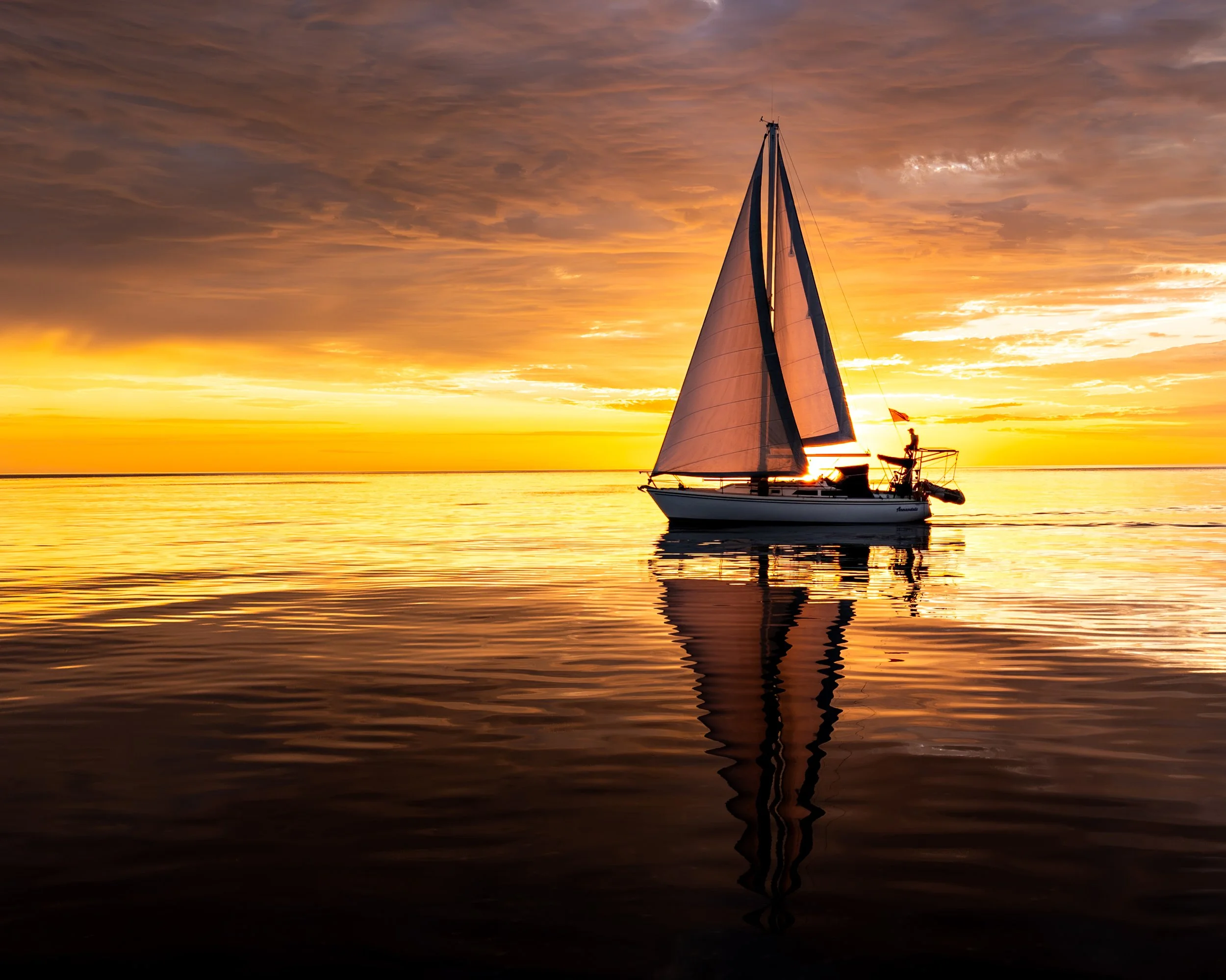 Sailboat on calm water at sunset with colorful sky and reflections.