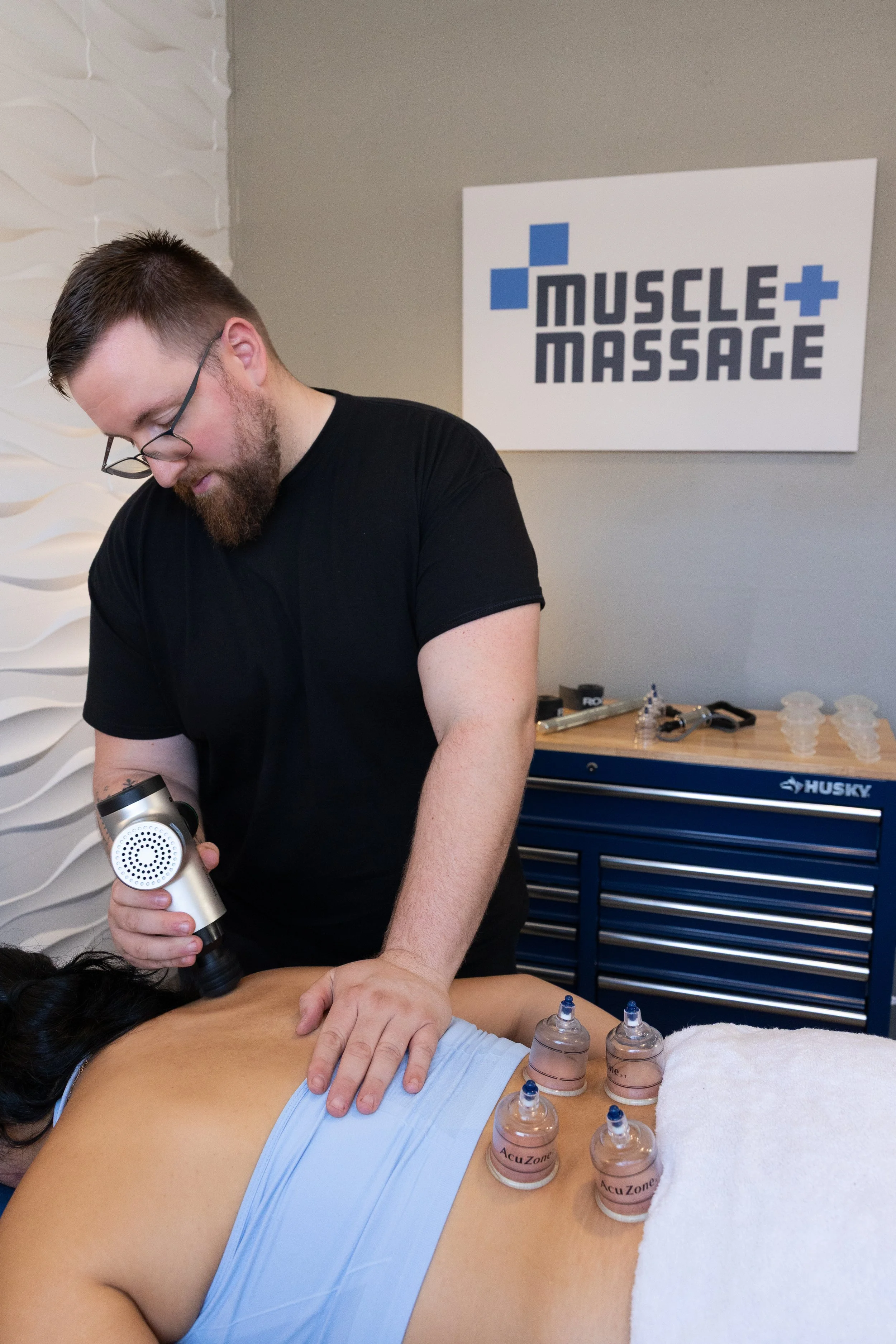 A man receiving a massage and therapy using cupping therapy on a woman's back in a treatment room.