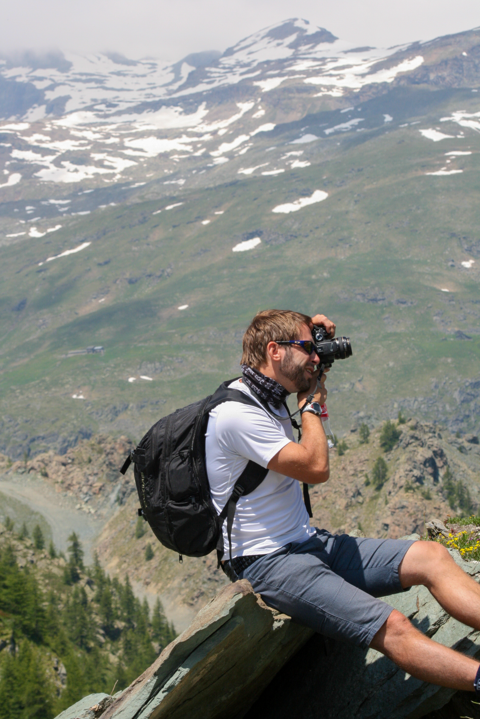 Man som sitter på en sten i berglandskap och fotograferar med kameror.