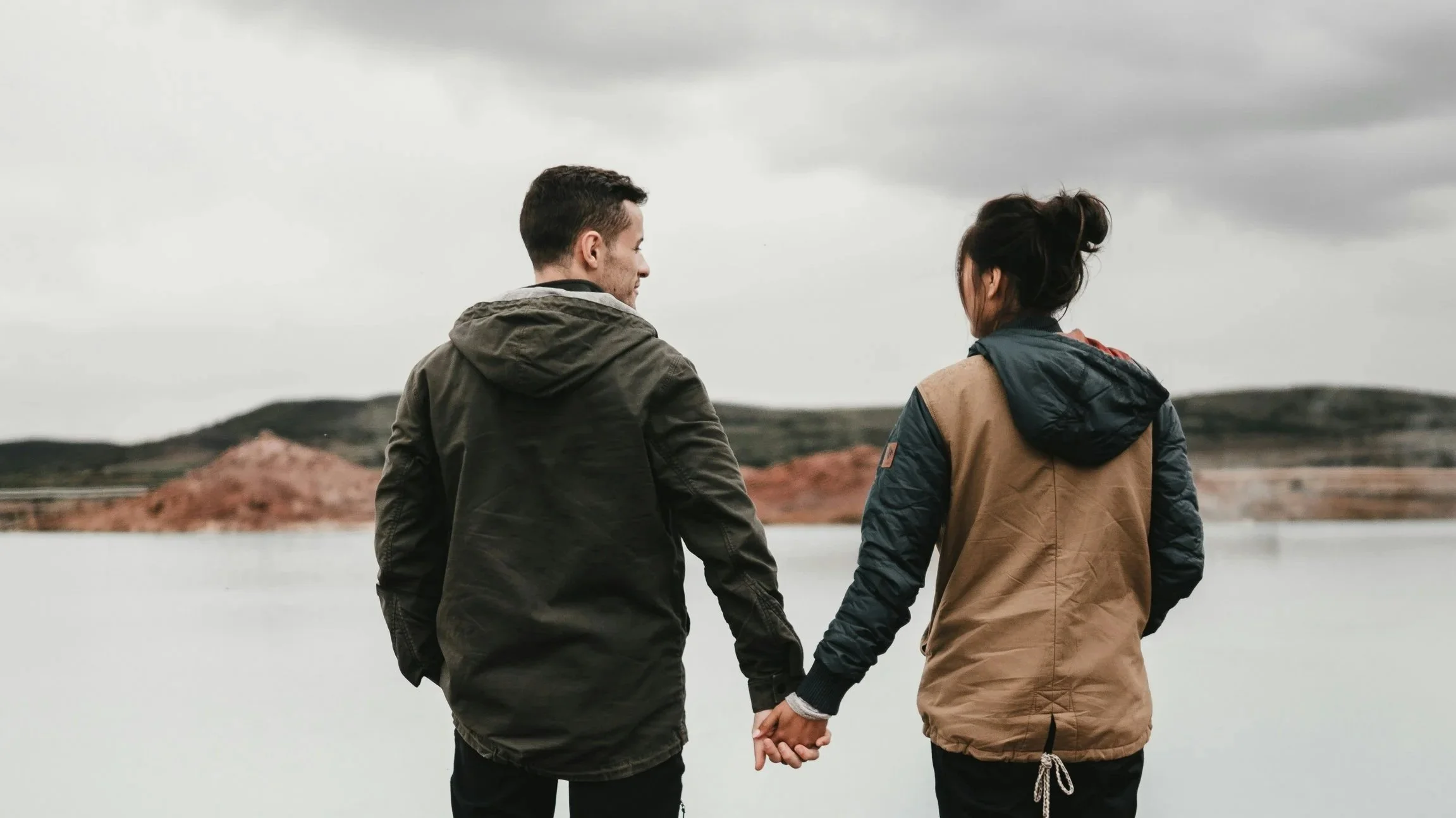 A photo taken from behind shows a couple standing together outside overlooking the water, perhaps contemplating their relationship strengths or marital issues.