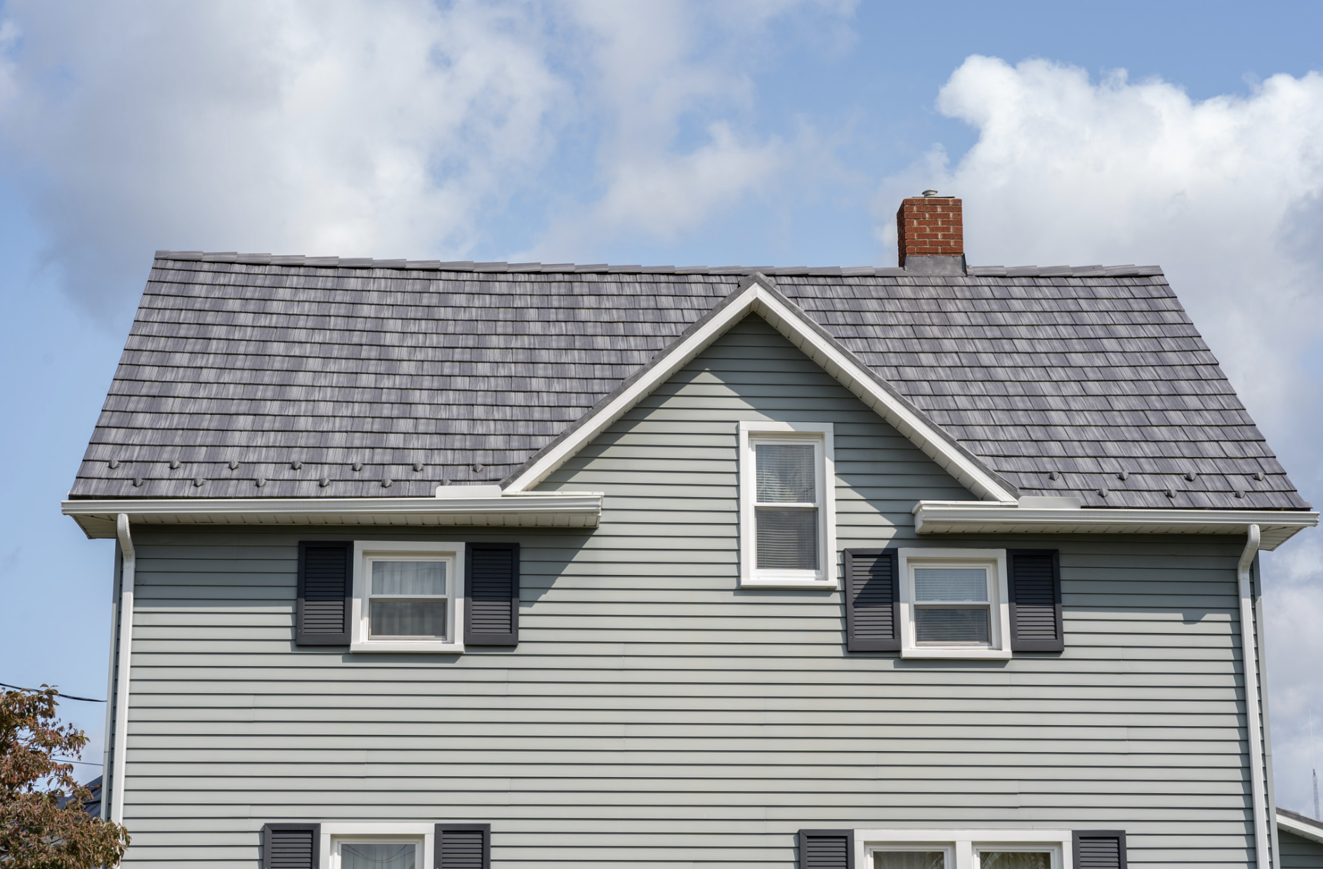 Front view of a house with gray siding, black shutters, and a gray shingled roof with a brick chimney.