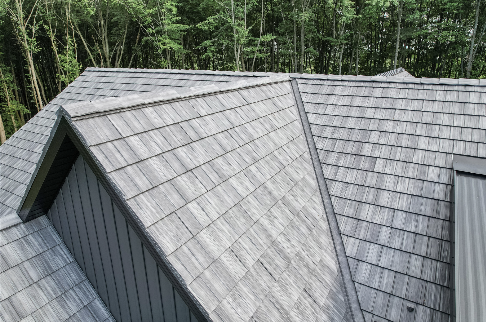 Aerial view of a house roof with gray shingles in a wooded area.