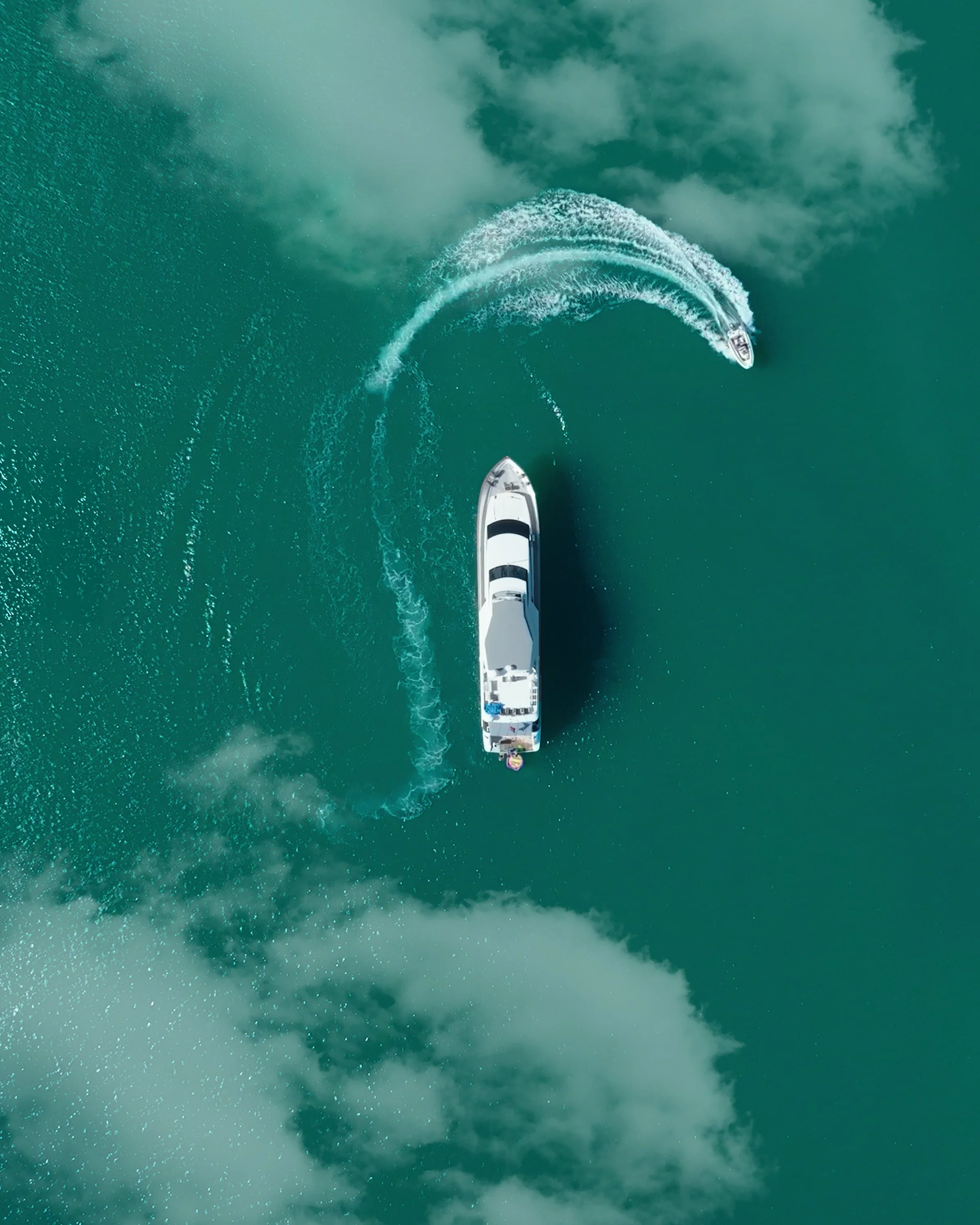 An aerial view of two boats in green water, creating wake trails as they move.