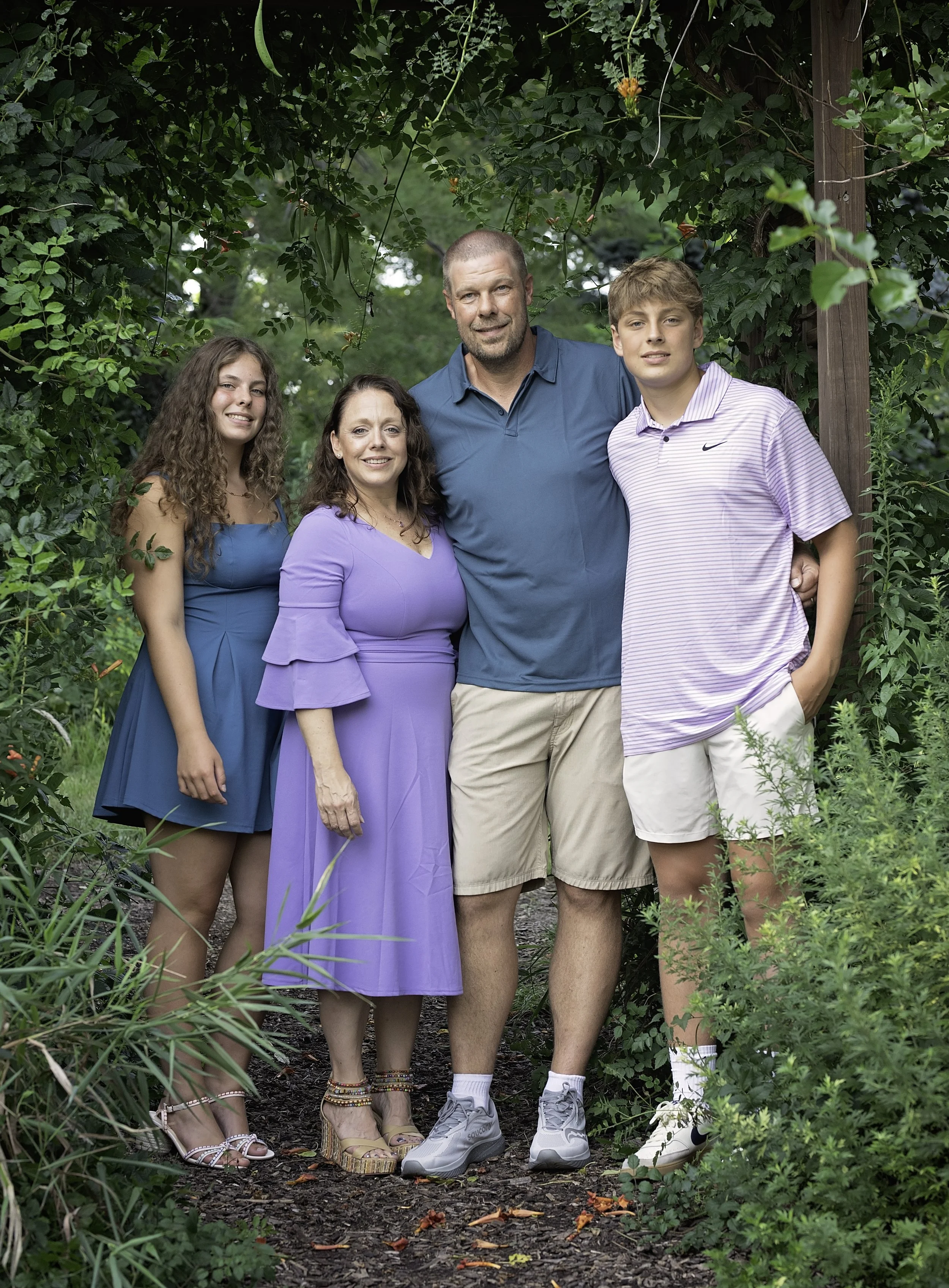 Family of five posing together outdoors in a lush garden with greenery and flowers.