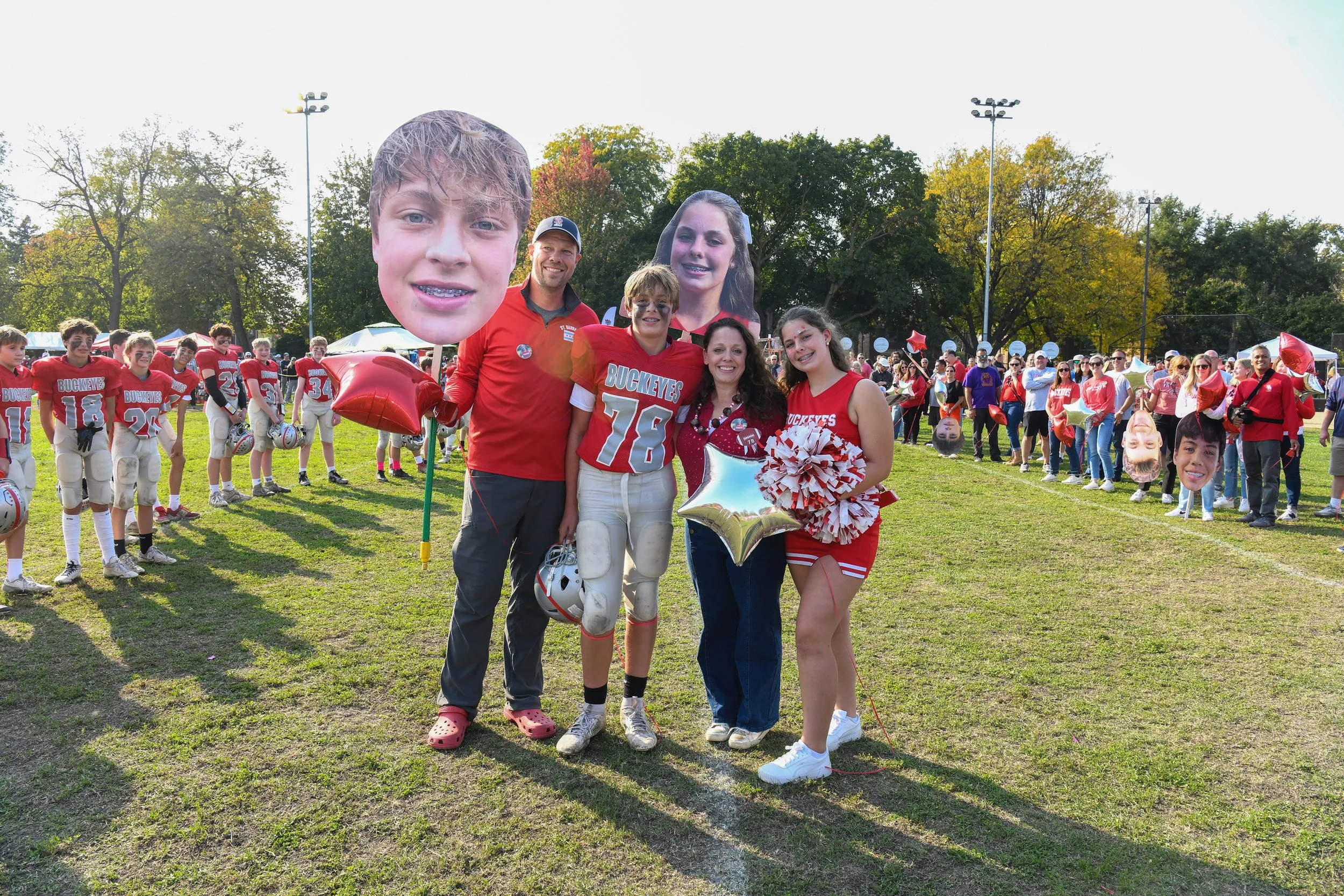 Group of people, including football players and cheerleaders, celebrating on a grassy field with balloons and masks posed for a photo.