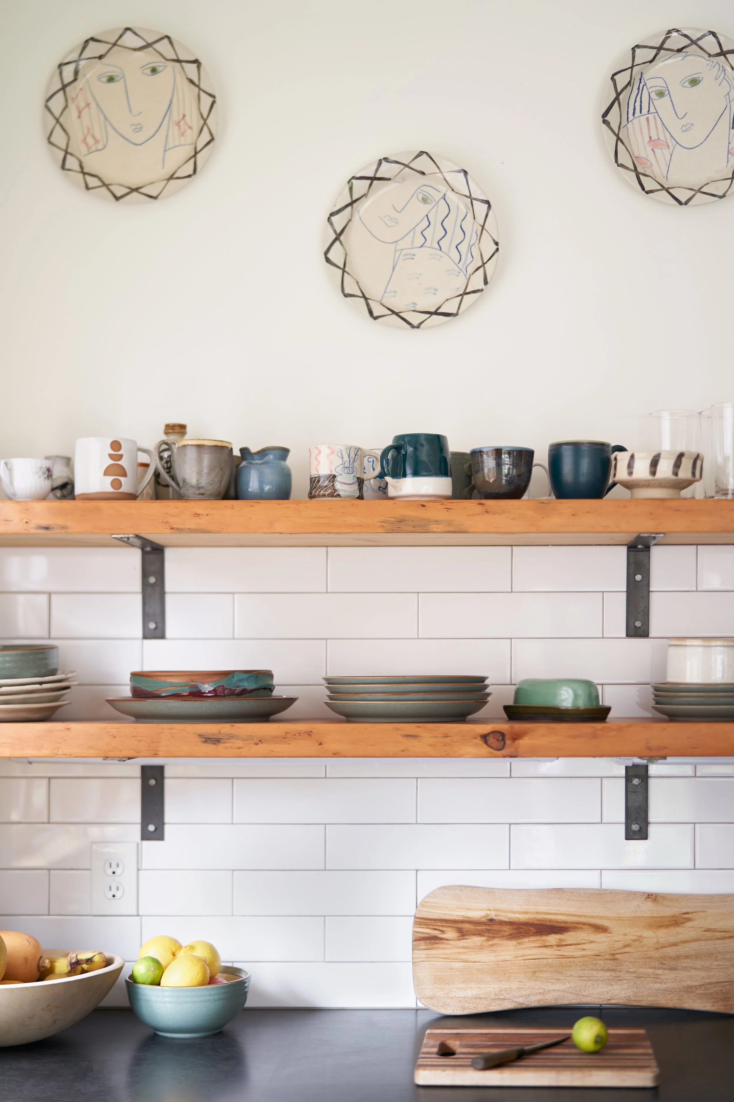 Simple wooden shelves in this remodeled kitchen are held by dark brackets and match the dark. countertops and cabinets and contrast nicely with the white tiled wall.