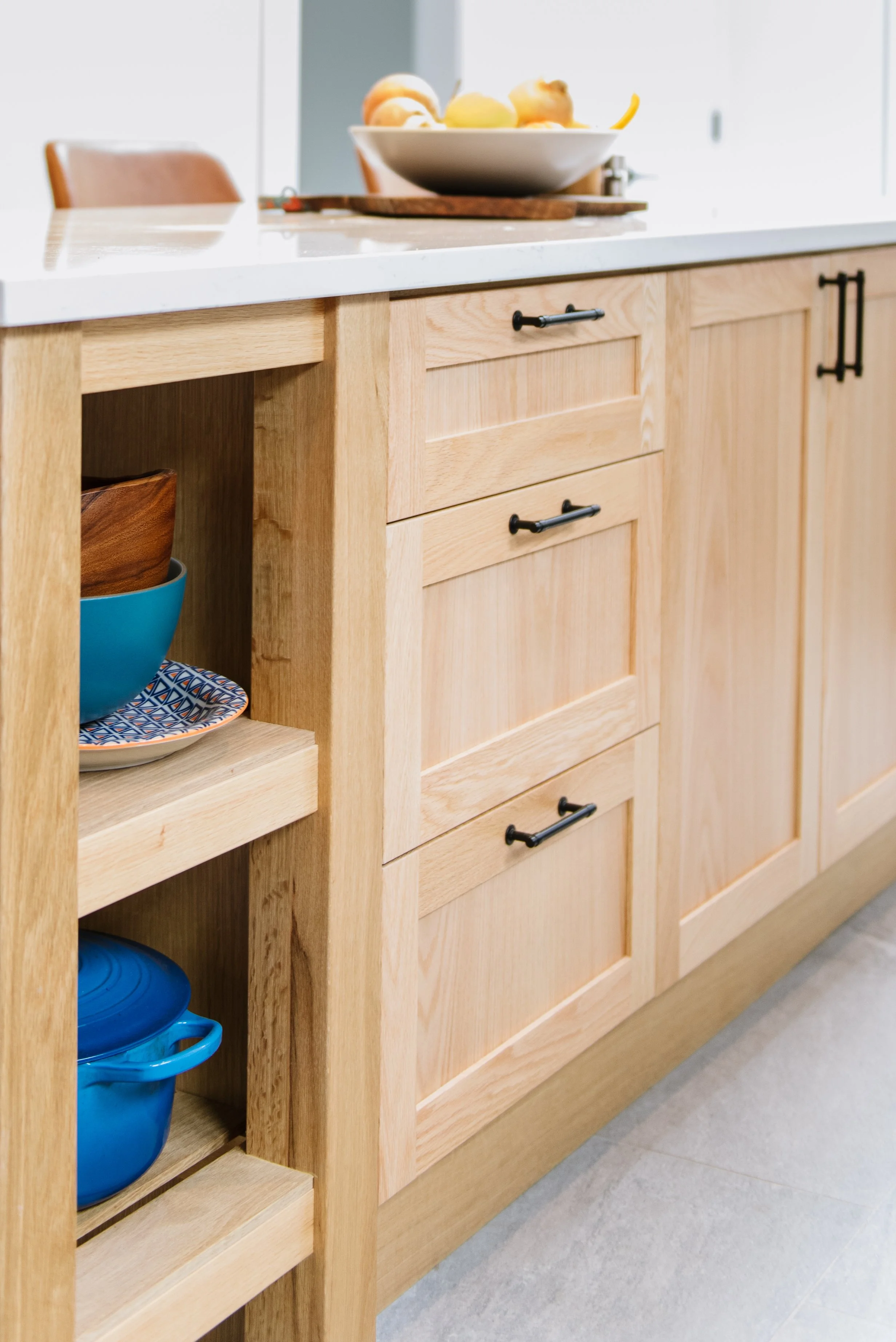 The new island in this kitchen design build project has open shelves, drawers, and cabinets with simple white counter.