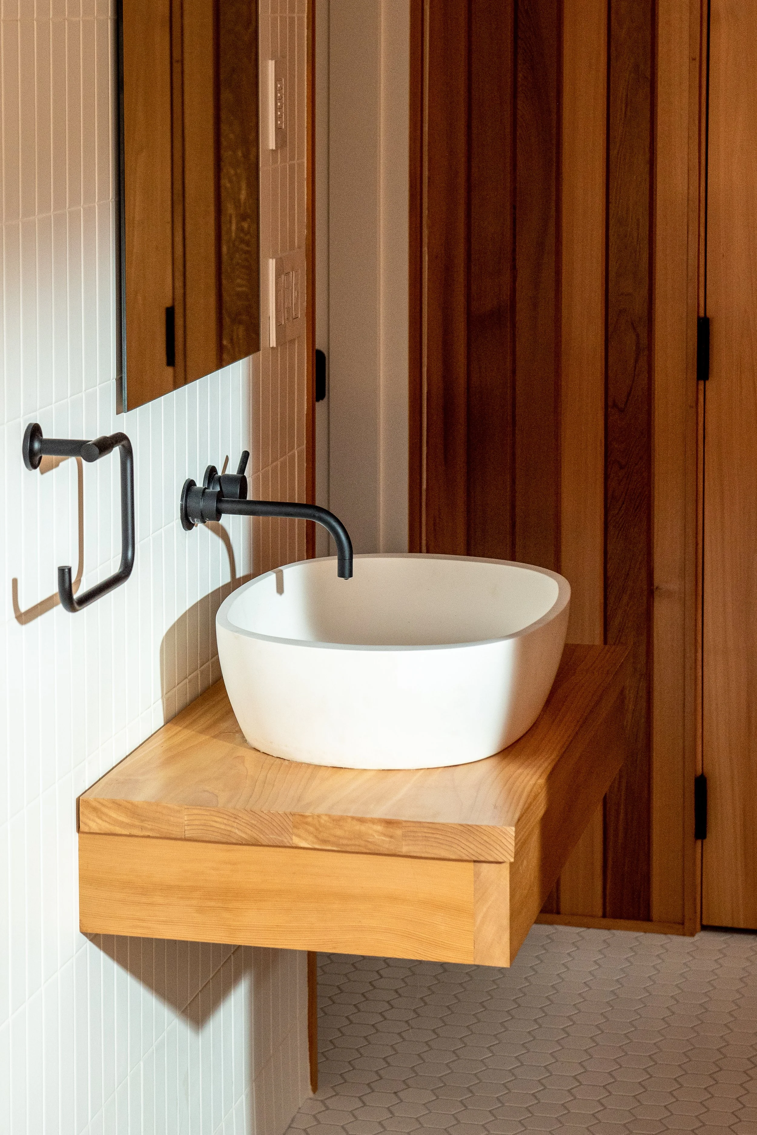 In this basement conversion, the new bathroom sink is an oval countertop white basin with dark metal faucets and fixtures, and rectangular mirror above.