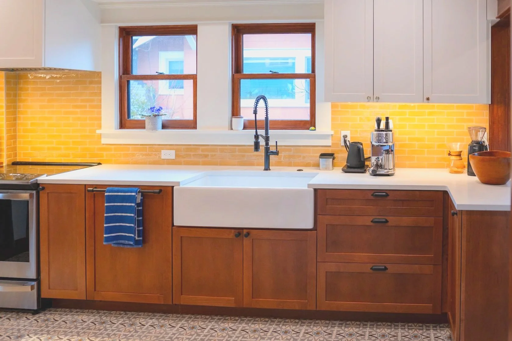 On the left is a stainless steel oven, white countertop, rectangular sink basin built into the dark wood cabinets, drawers and dark metal hardware and fixtures.