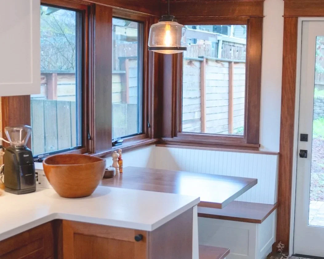 Rich wood toned cabinets and window trim and white countertops and walls make a seamless transition from the kitchen to the newly remodeled seating area.