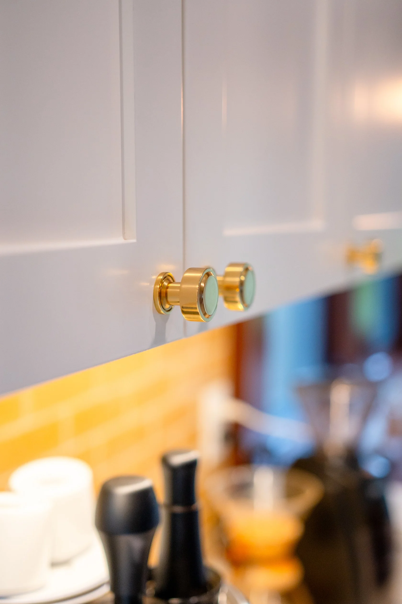Remodeled white cabinets above the counter have round gold-toned knobs to match the. yellow wall tile.
