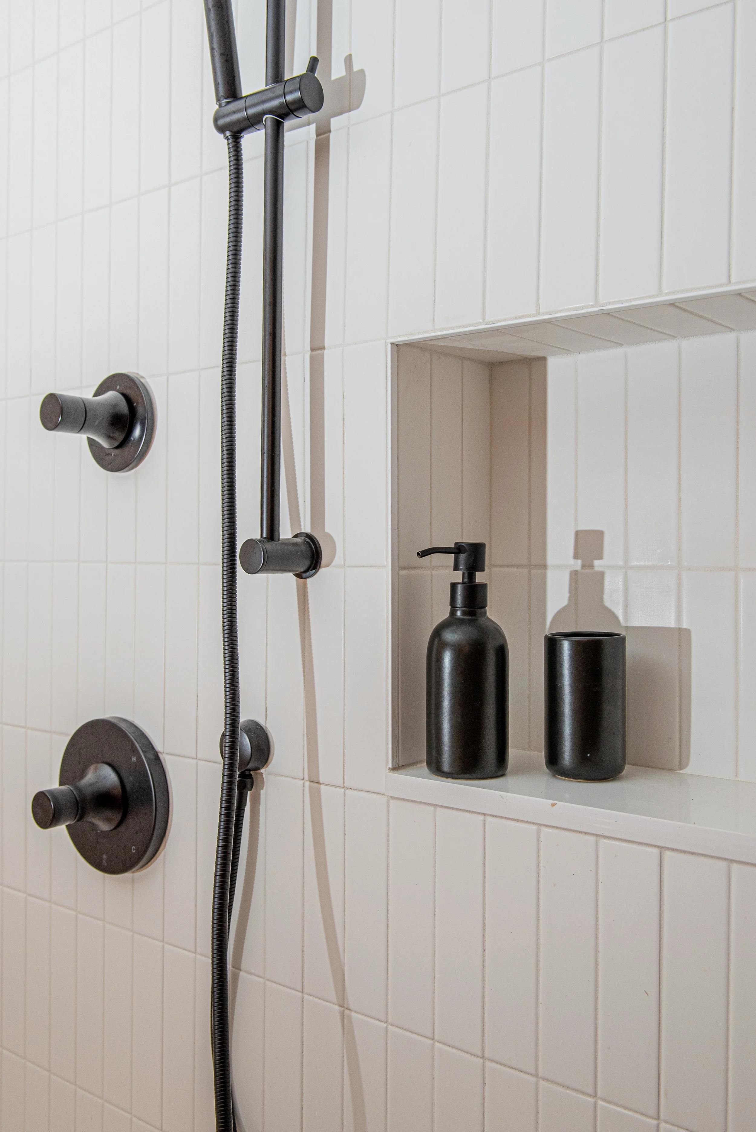 The design build team created a white tiled shower with dark fixtures and a small nook for shampoo and soap along the wall.