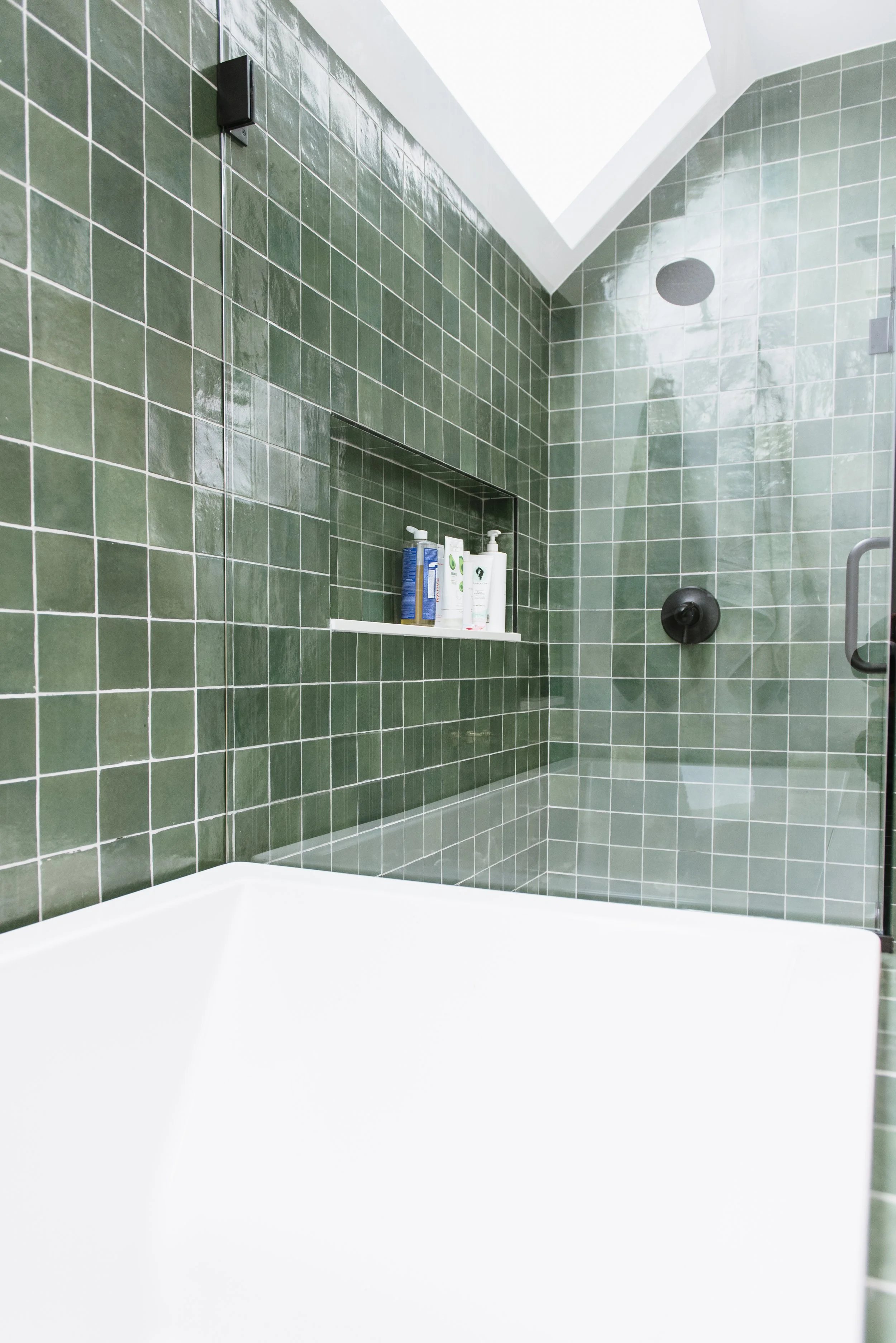 Renovated bathroom with white walls and green tiled shower next to the bathtub.