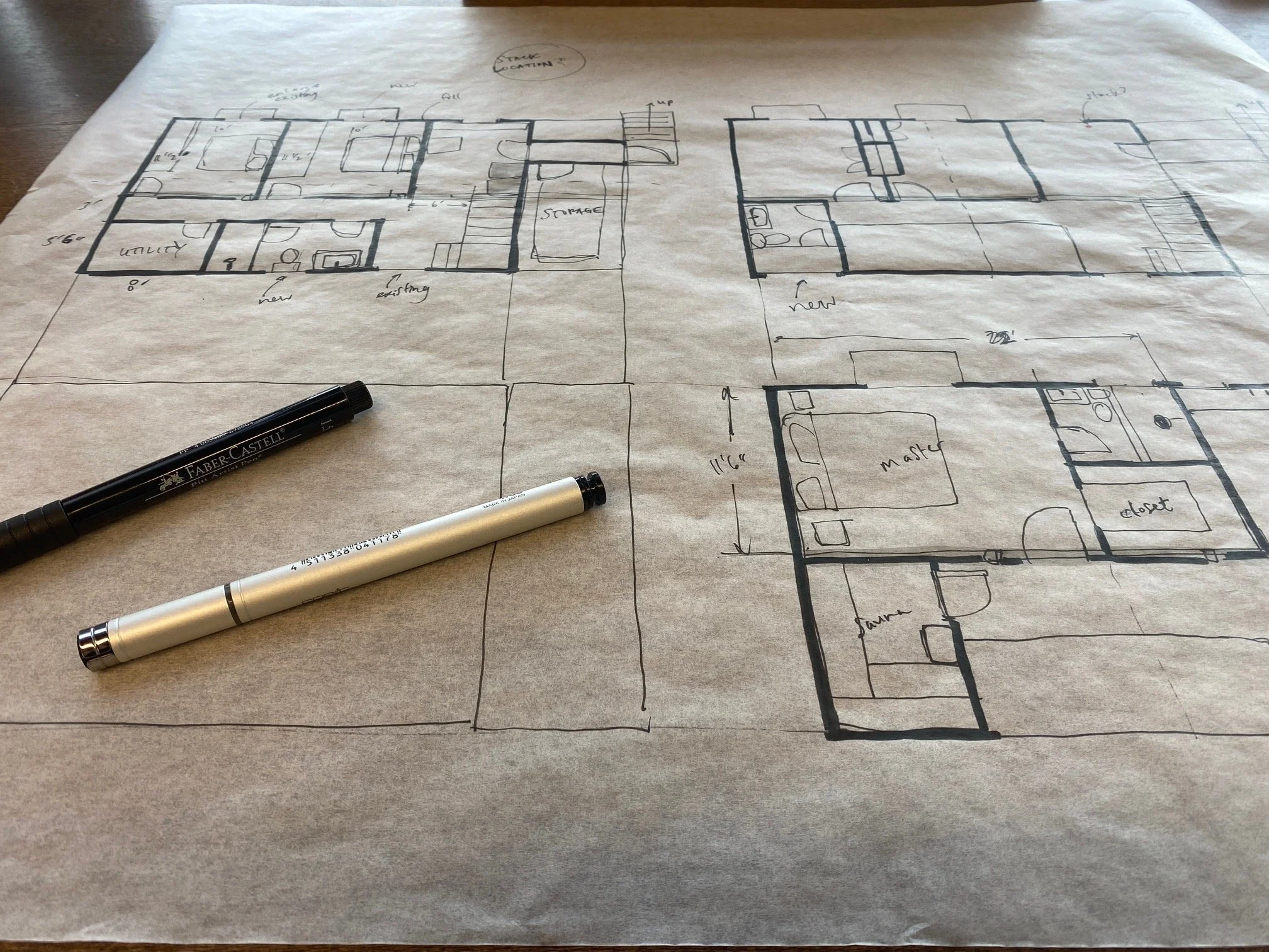 A hand-drawn floor plan on paper depicts multiple rooms with annotations. Markers are placed on the table, including a black Faber-Castell marker and a silver pen.