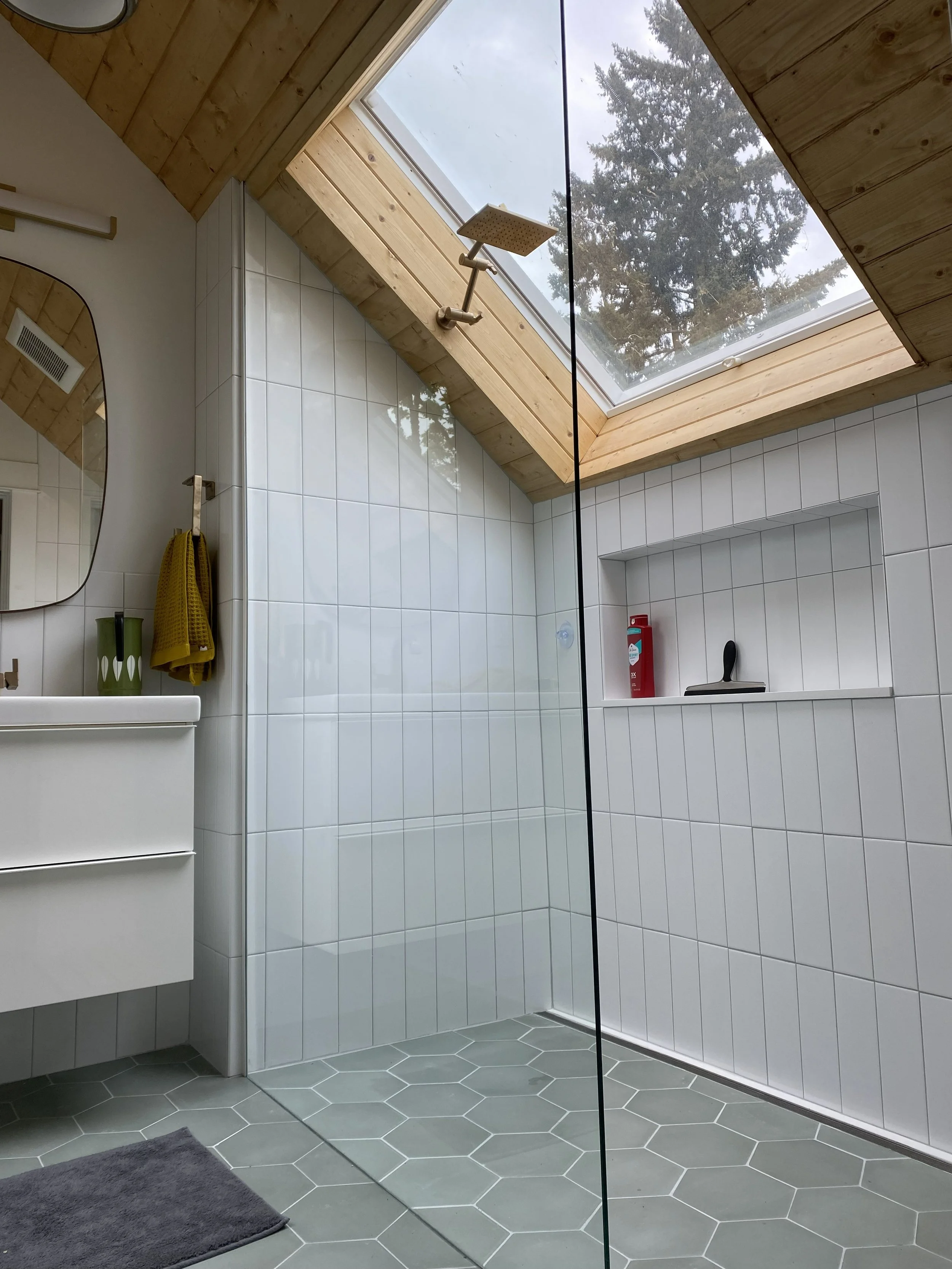 Bathroom with large skylight window in ceiling, white tiled walls, gray hexagonal floor tiles, and a gray bath mat on the floor.