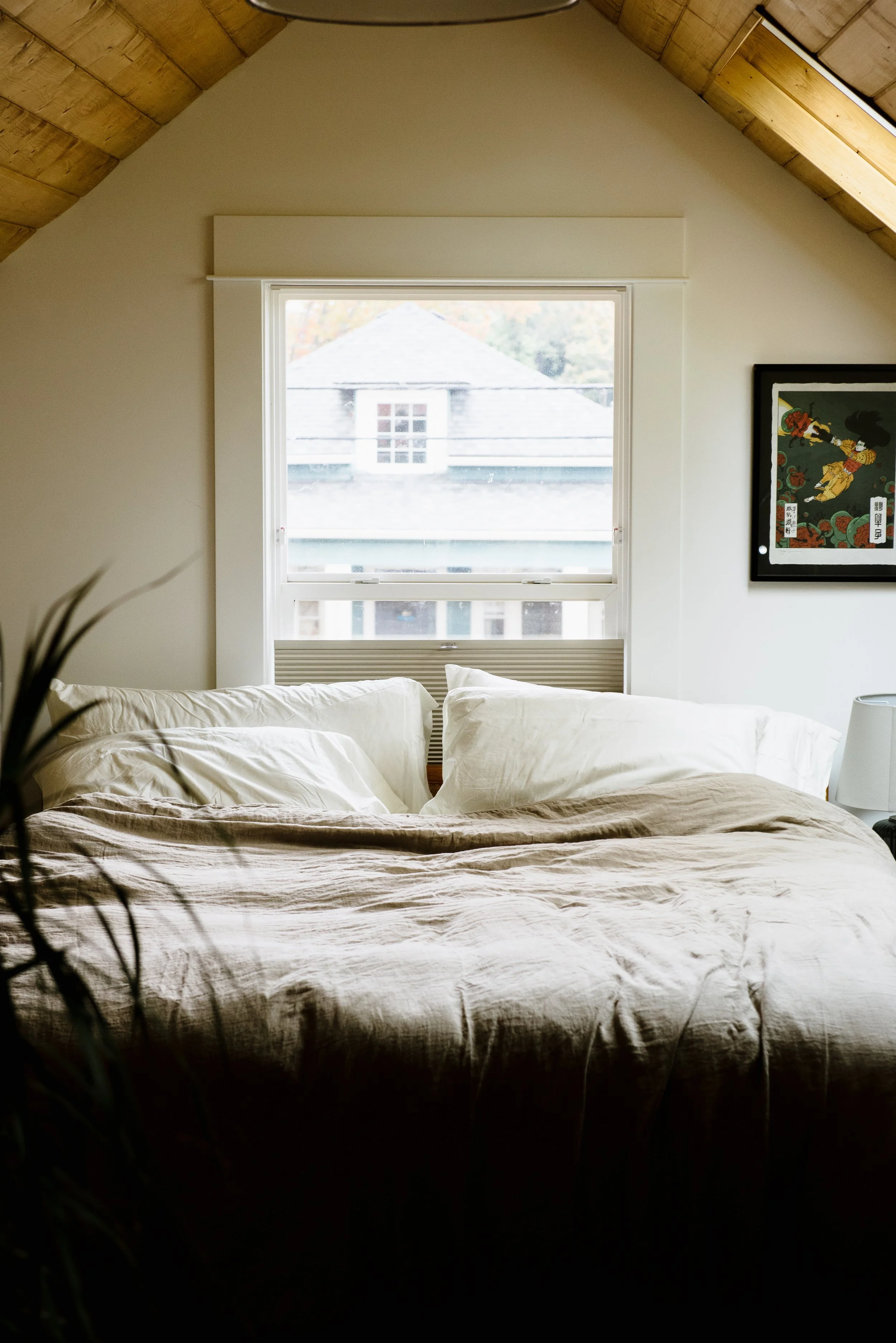 This primary attic bedroom conversion's A-framed ceiling frames a window over the bed. The window has a top down bottom up shade to maintain a view and natural light, without compromising your privacy.
