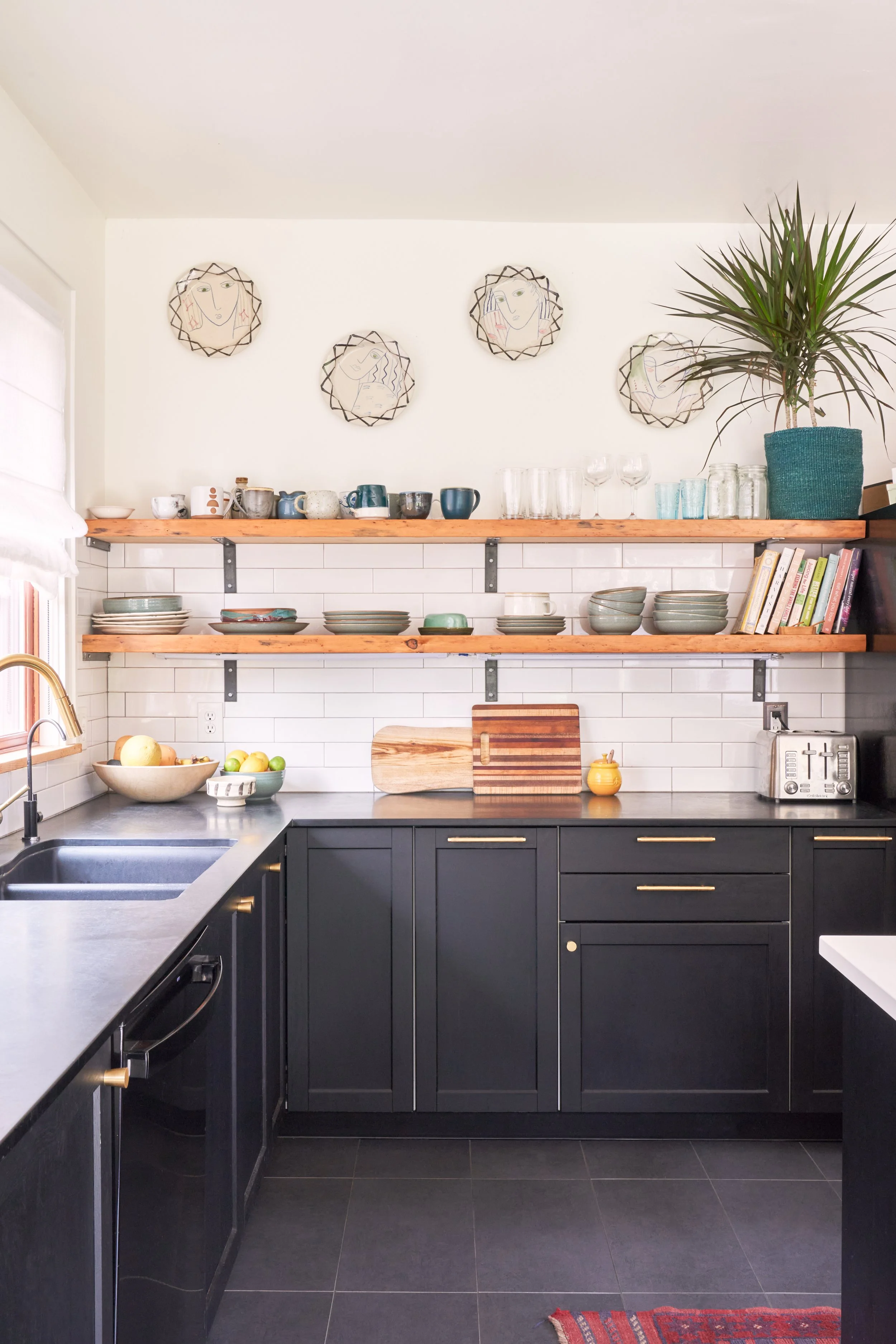 A modern kitchen with black cabinets, open wooden shelves, white subway tile backsplash, and decorative wall art.