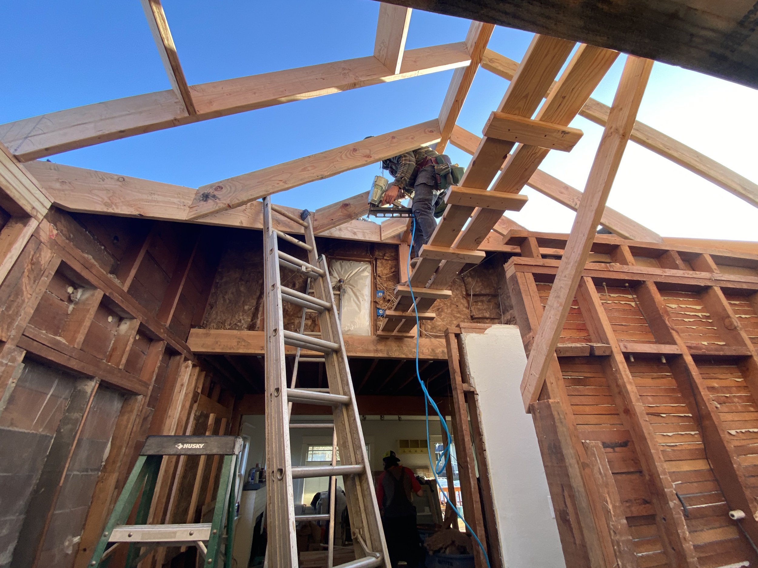 Construction worker standing on a scaffolding inside a house under renovation, where the wooden framing for the roof is being built.