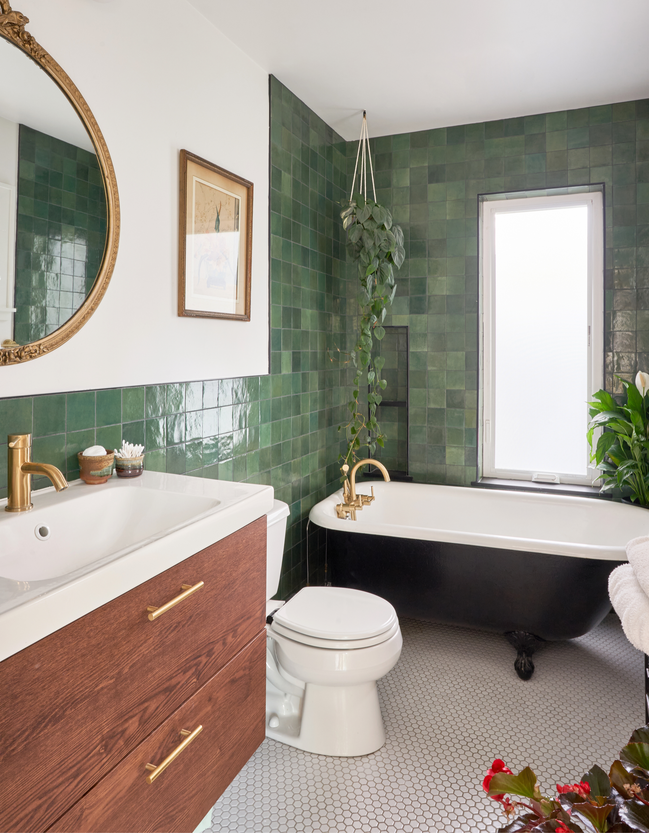 The design build team gave this bathroom a more cozy feel with the clawfoot tub, green tile, round mirror, and white sink, and wood cabinets.