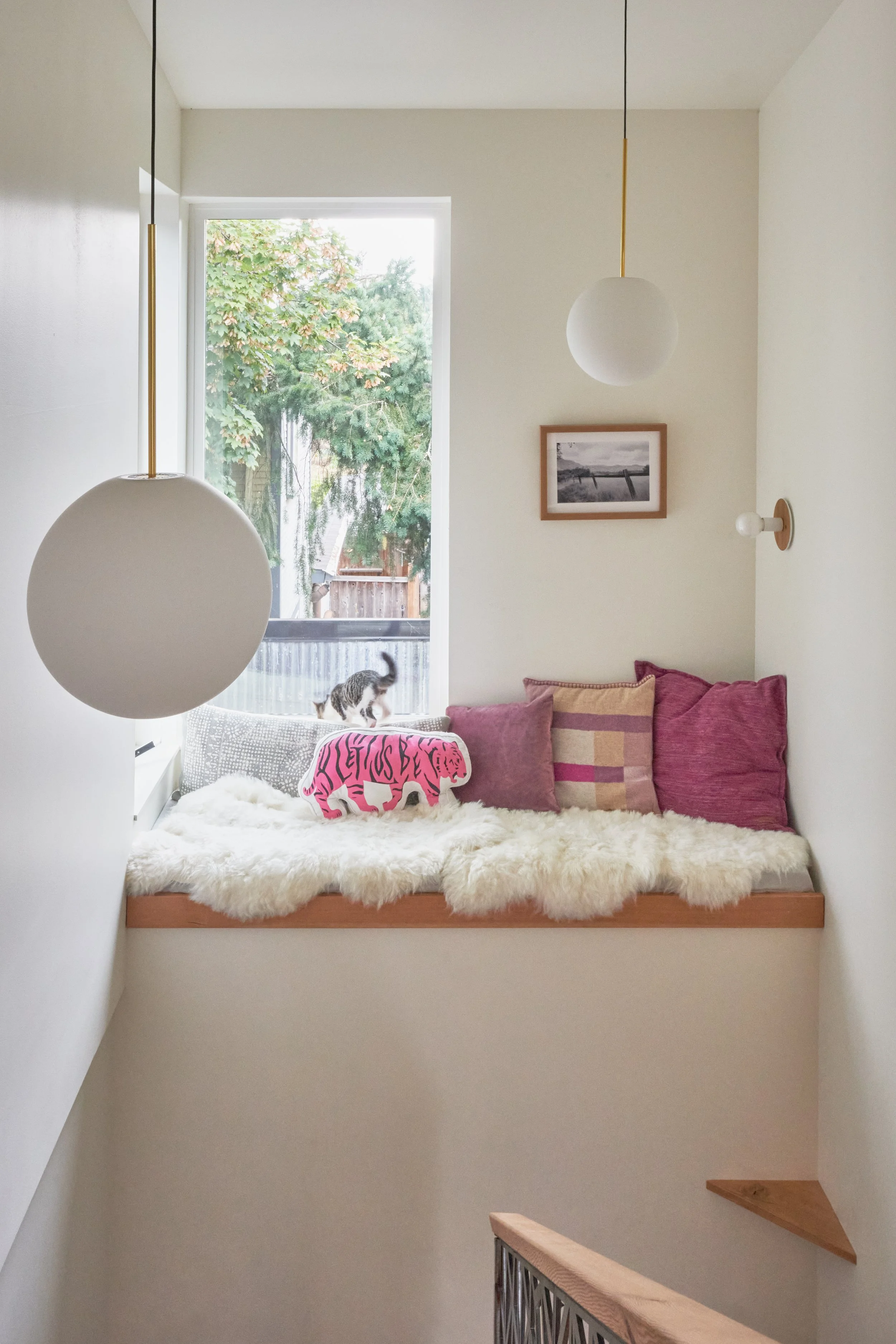 For this home remodel, our designer chose spherical hanging lights that contribute to the whimsical feeling of this bay window seat with pink pillows and a white furry blankets.