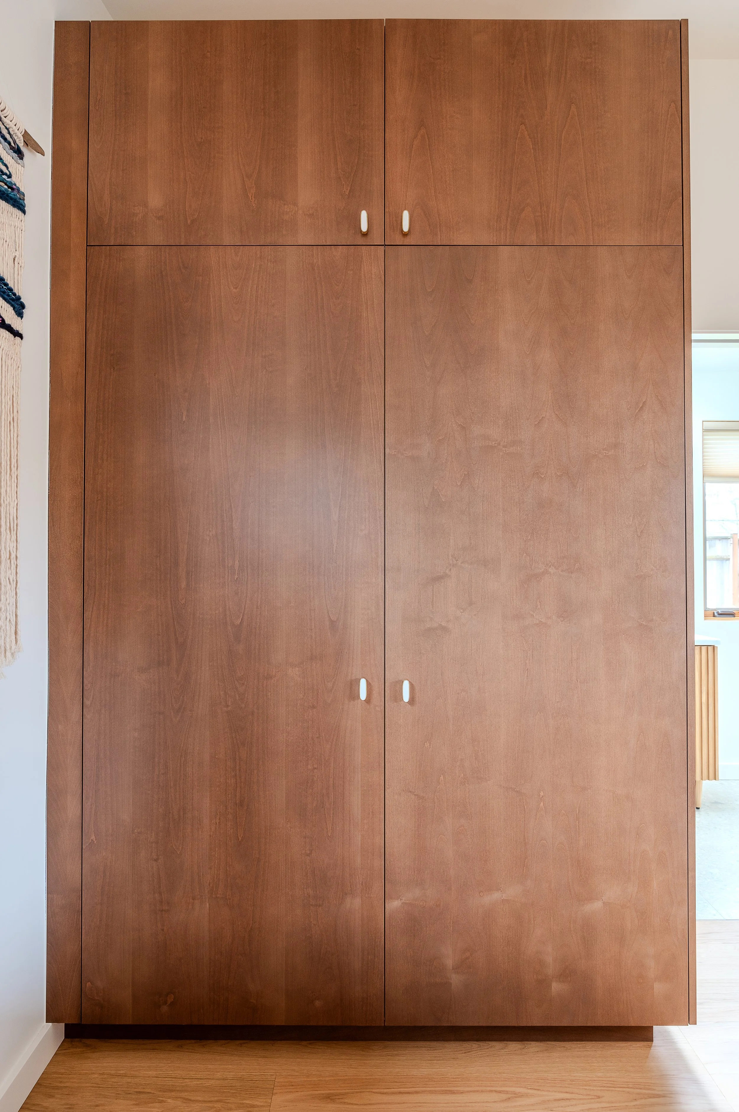 A large wooden cabinet with four doors, two smaller ones on top and two larger ones below, with white handles. It is part of a modern ADU bathroom, built to maximize storage space.