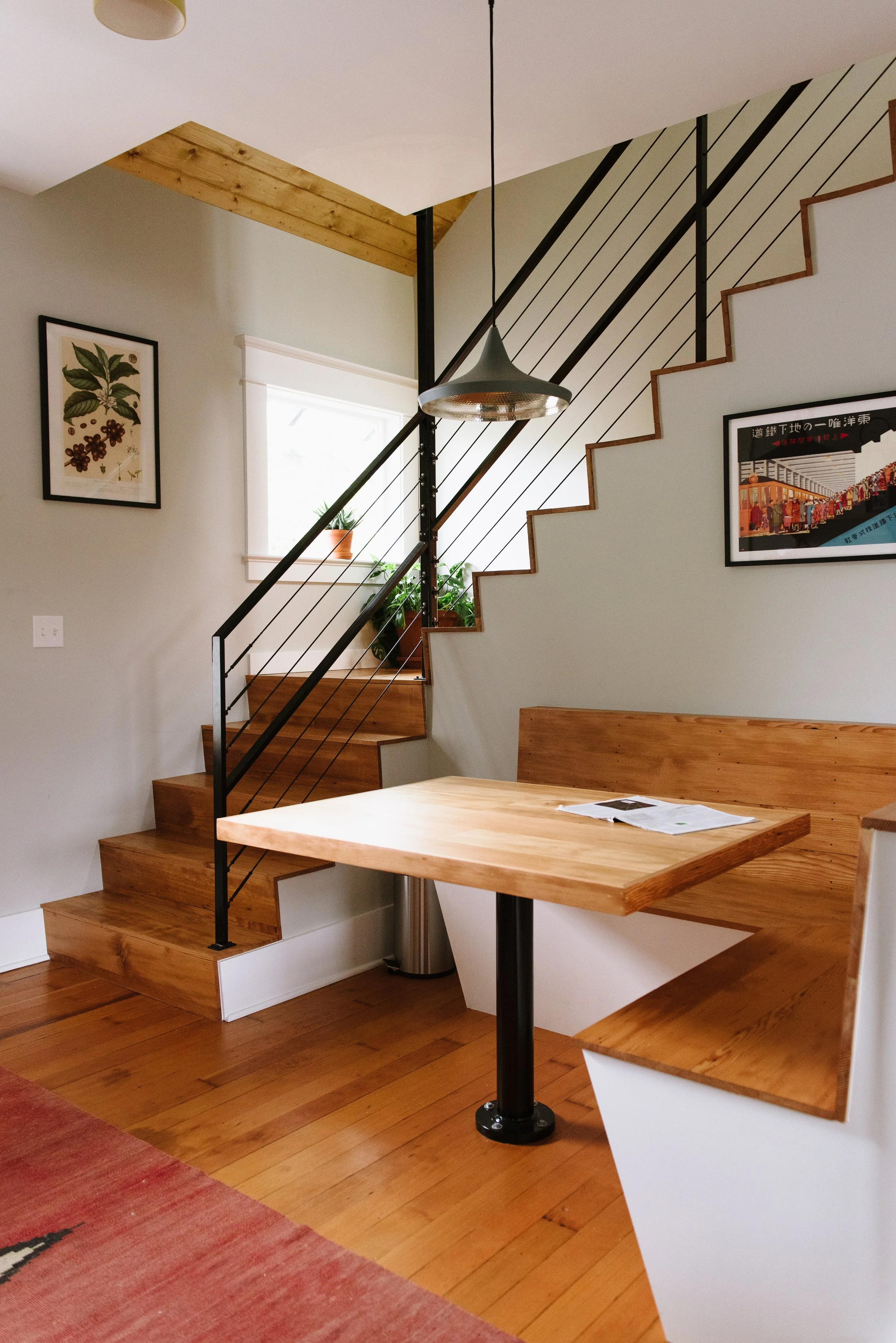 The stairs down from the renovated attic are open on one side, have a window in one of the walls opposite where the stairs turn, and lead down to a custom seating banquette.