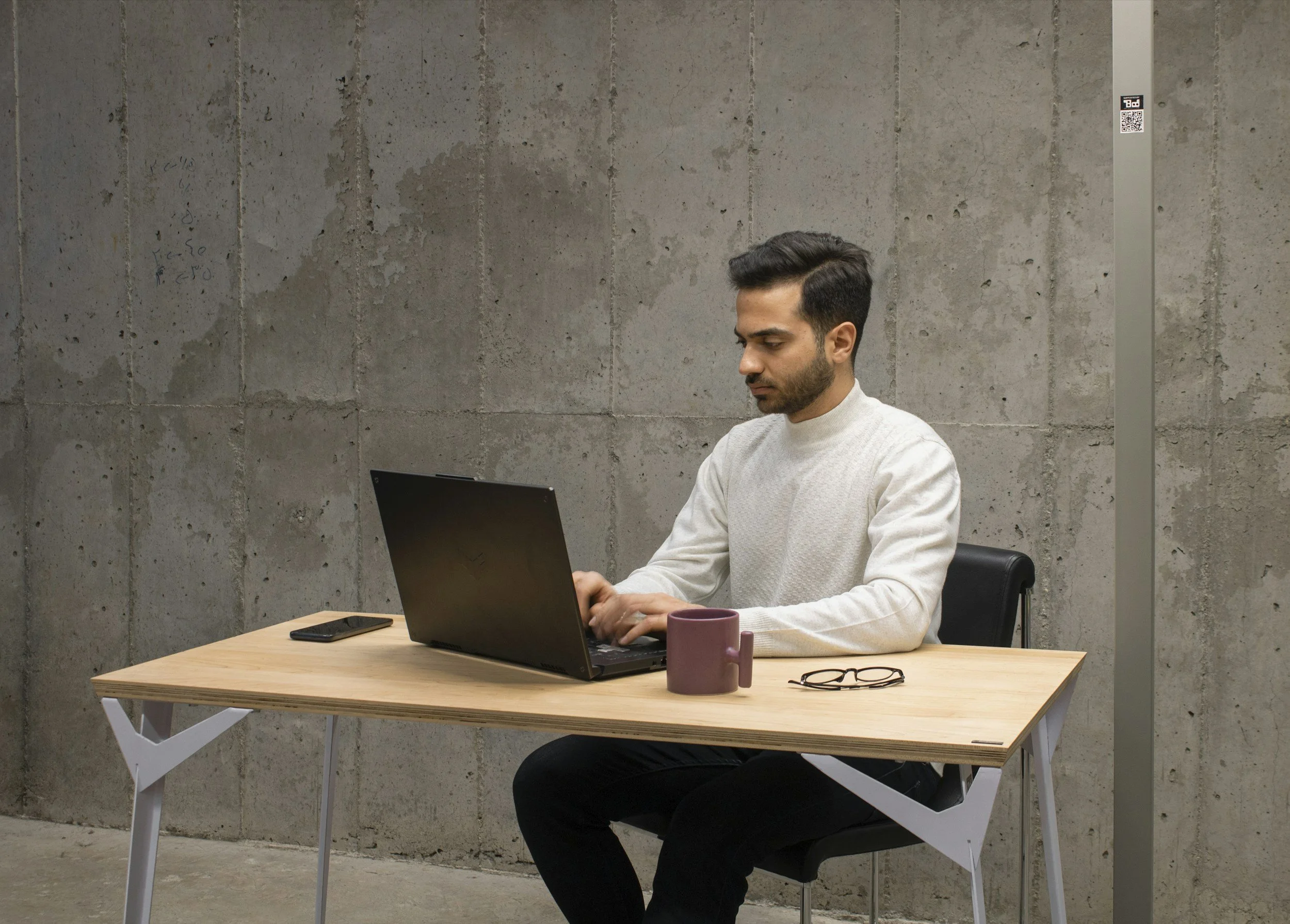 A man with black hair and beard in an office setting in front of a laptop