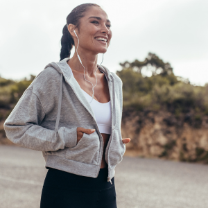 Woman smiling in workout attire outdoors with earbuds